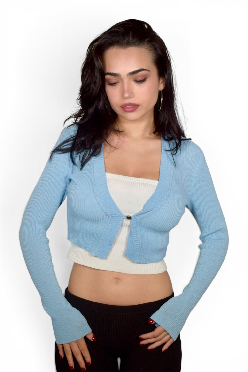 Woman wearing a light blue cardigan over a white top and black pants on a white background