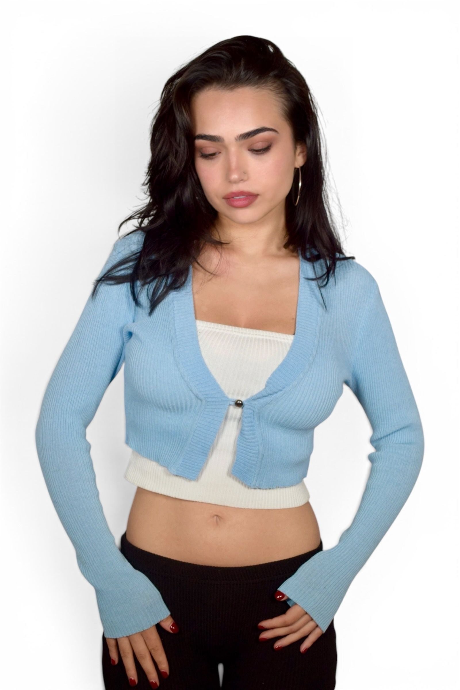 Woman wearing a light blue cardigan over a white top and black pants on a white background