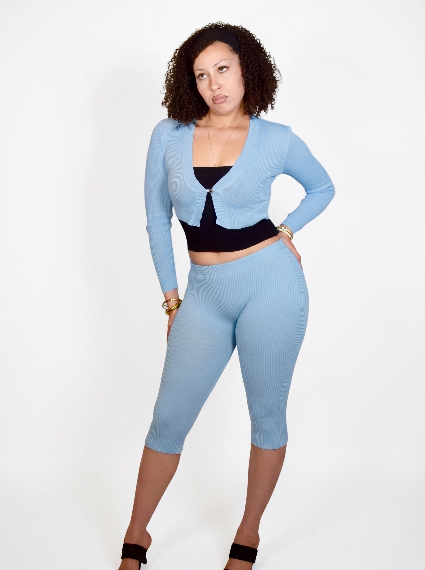 Woman wearing a light blue long-sleeve top and capri leggings on a white background