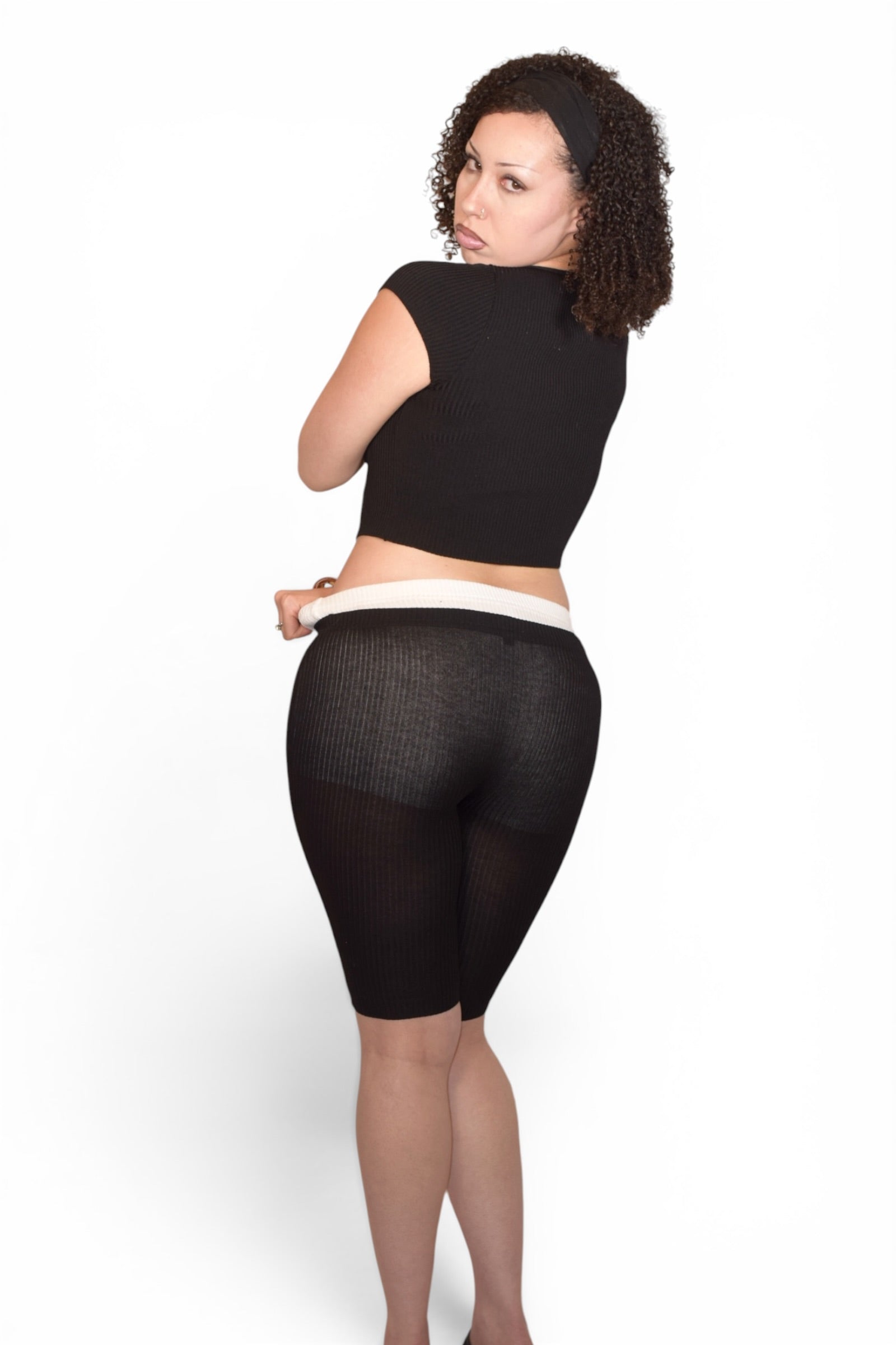 Woman wearing black tights and a black crop top on a white background