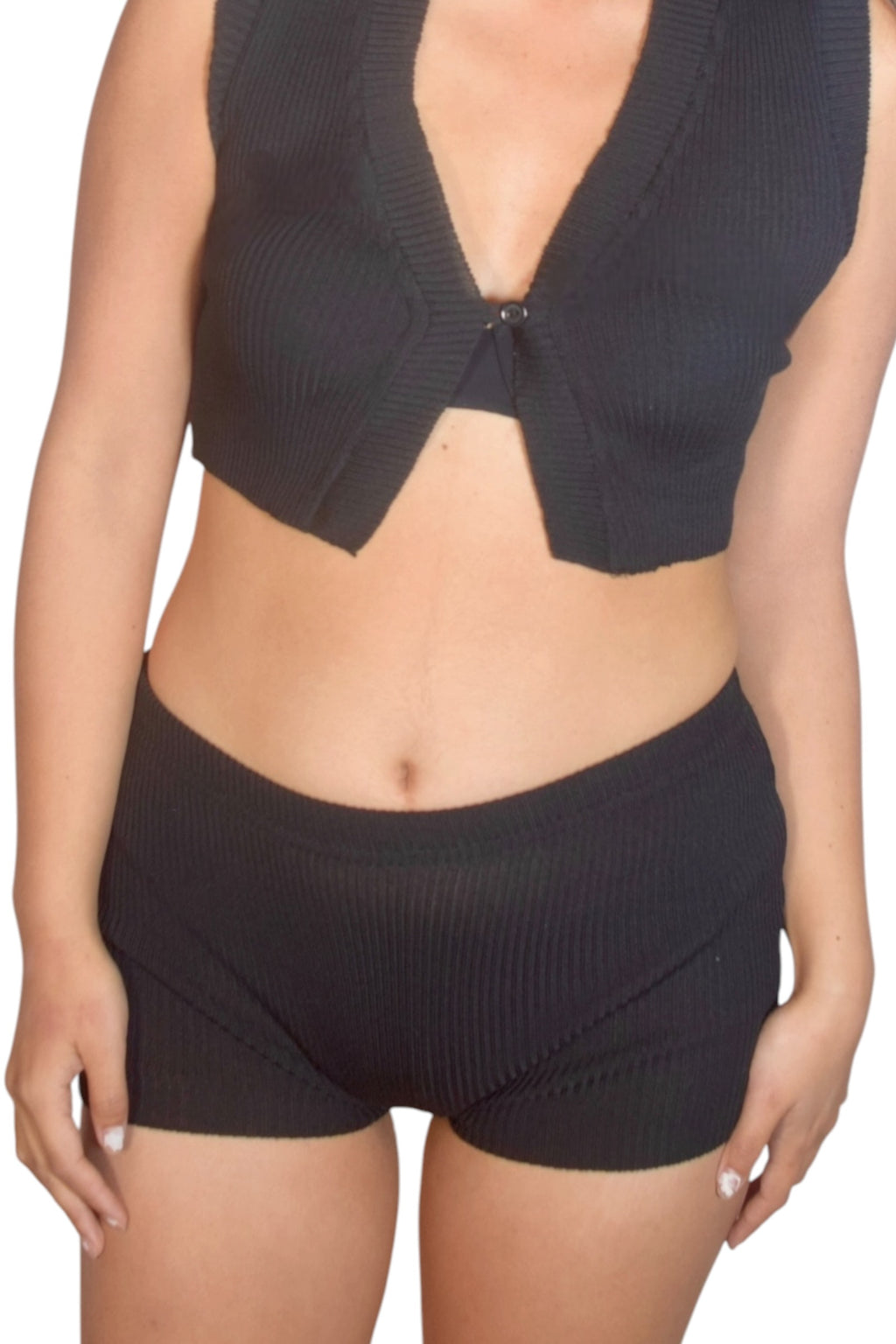 Person wearing a black ribbed crop top and shorts set on a white background