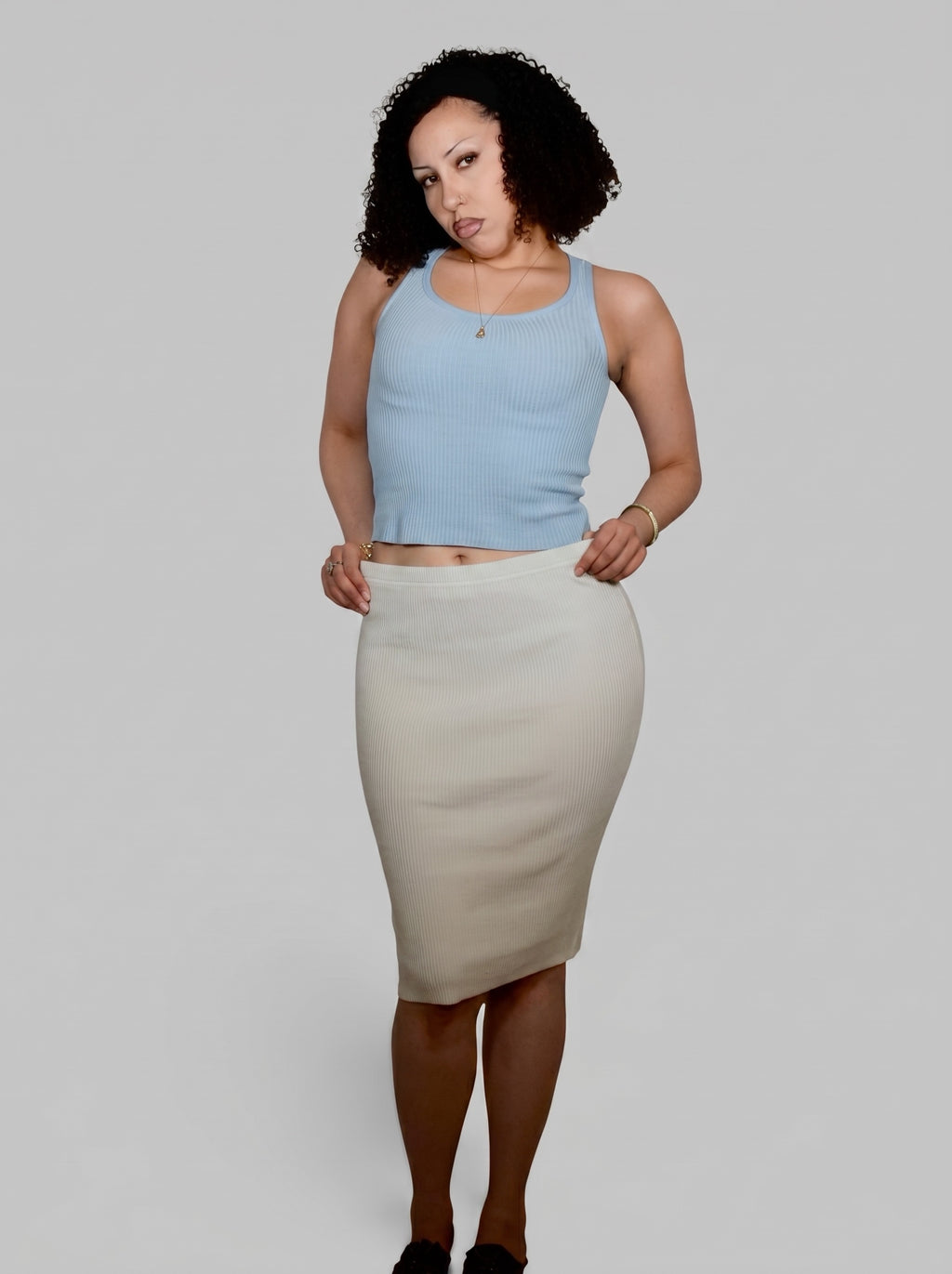 Woman wearing a light blue top and beige skirt on a plain background