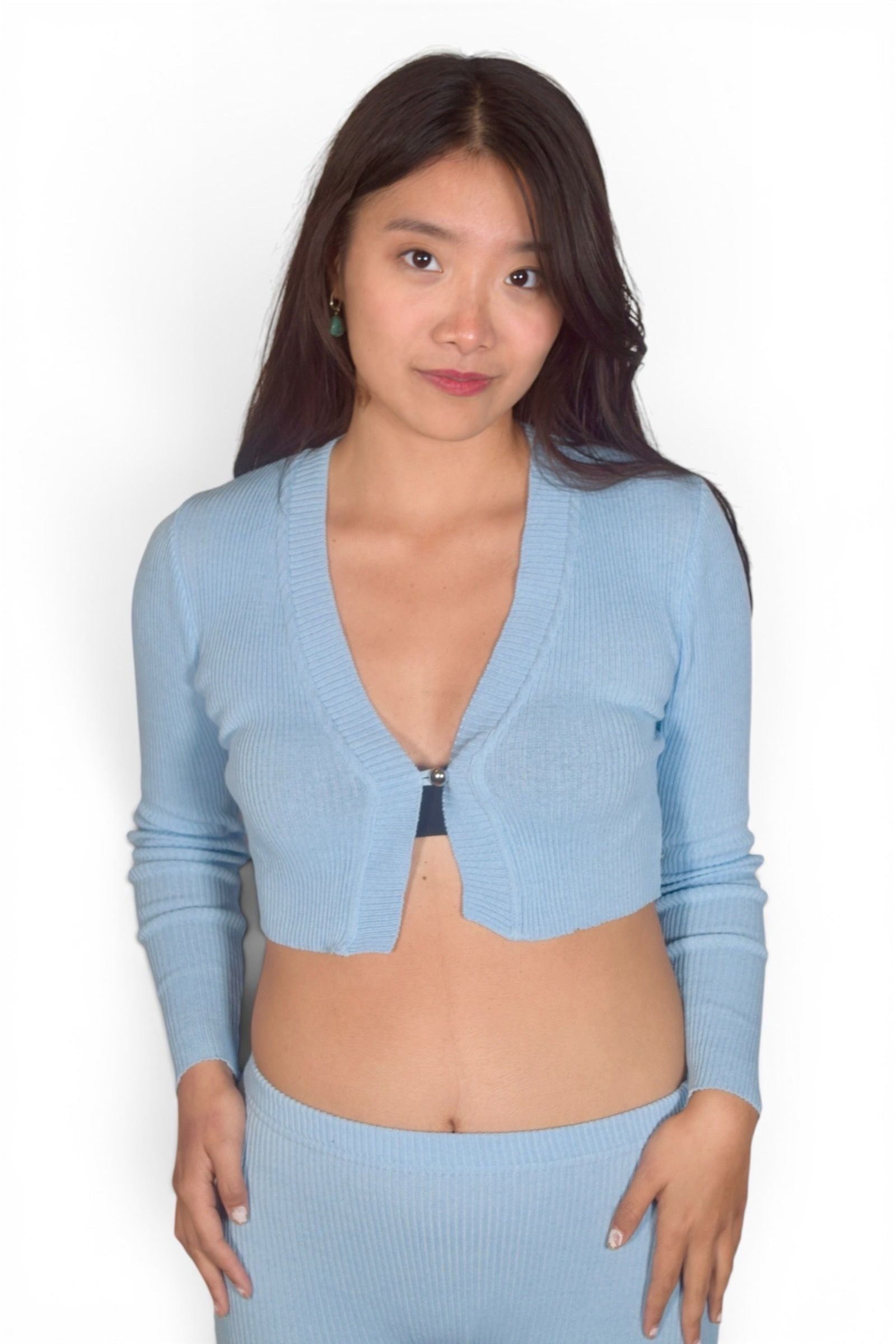 Woman wearing a light blue ribbed cardigan over a matching outfit on a white background