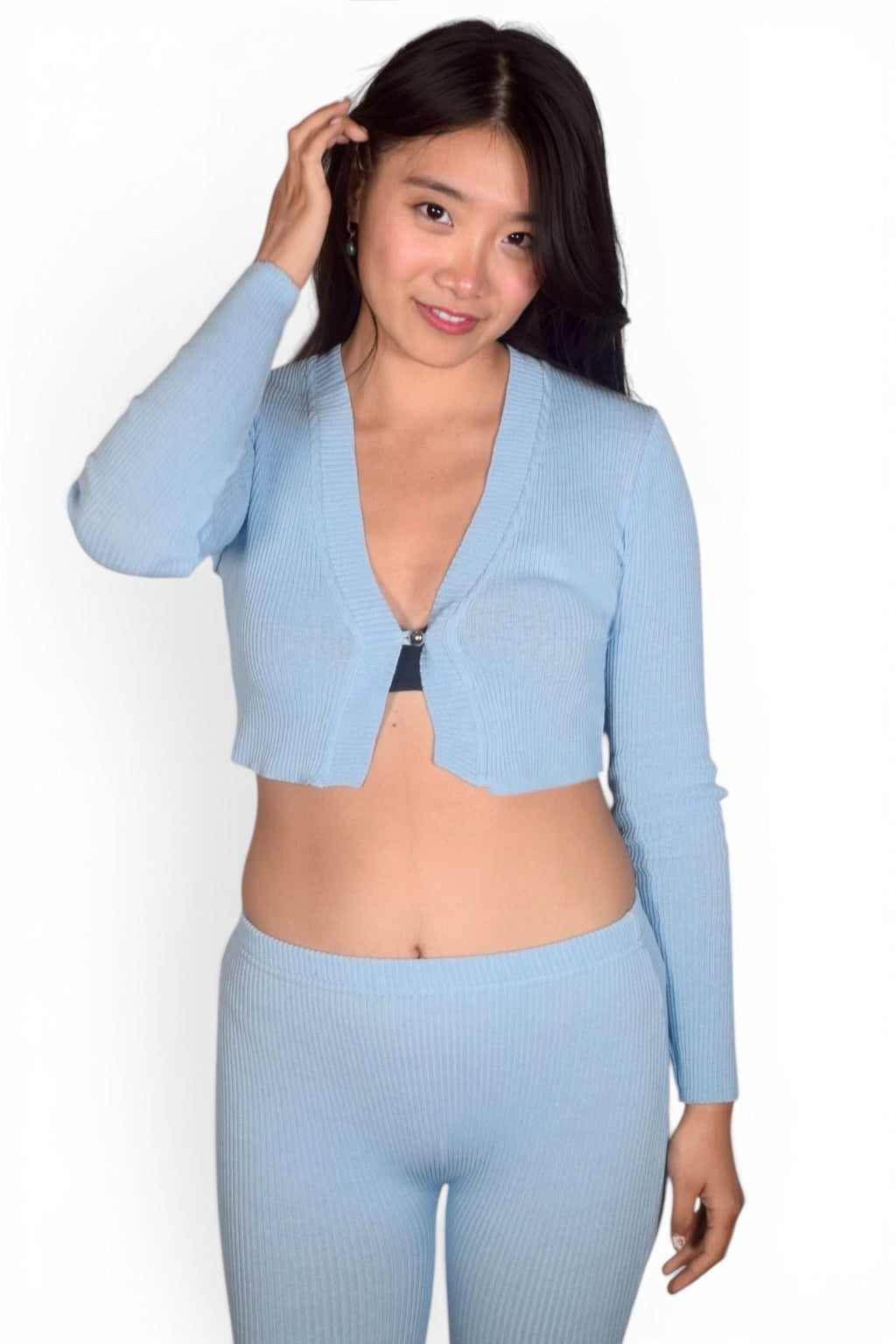 Woman wearing a light blue cropped cardigan and leggings against a white background