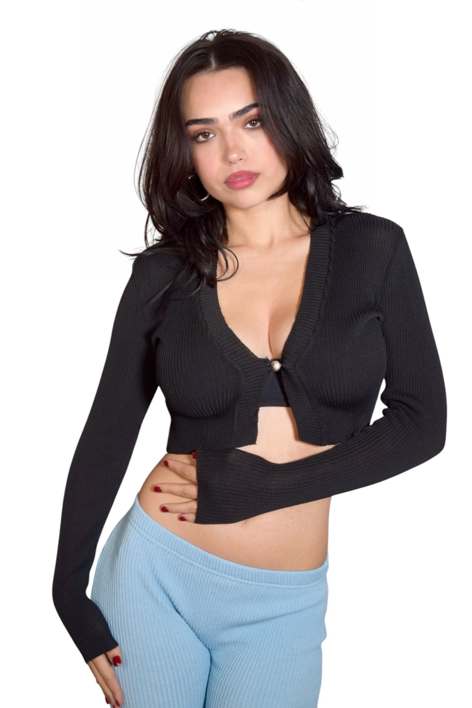 Woman wearing a black long-sleeve top over a beige garment with light blue pants on a white background