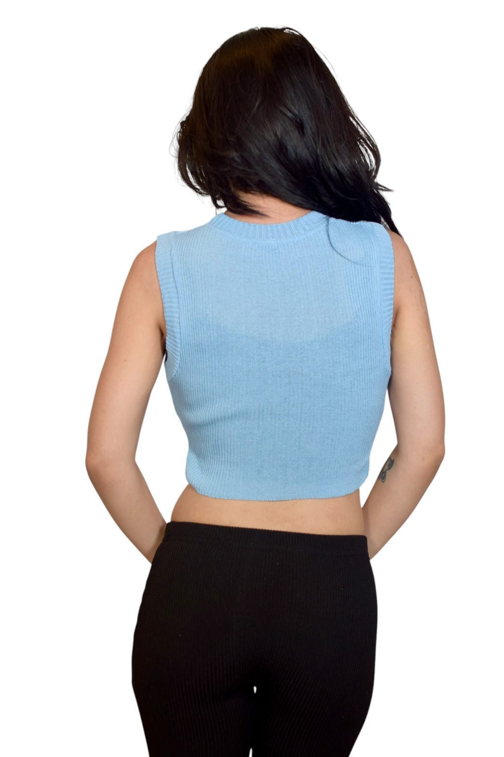 Person wearing a light blue sleeveless top and black pants on a white background