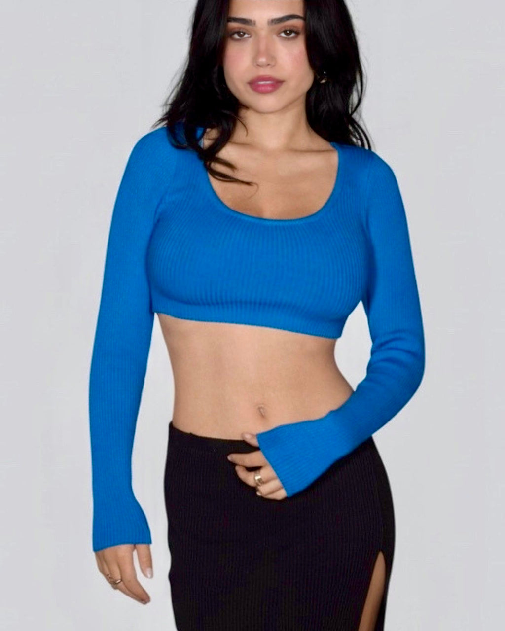 Woman wearing blue crop long sleeve rib knit top with blk skirt with slit by The Knit House LA. 