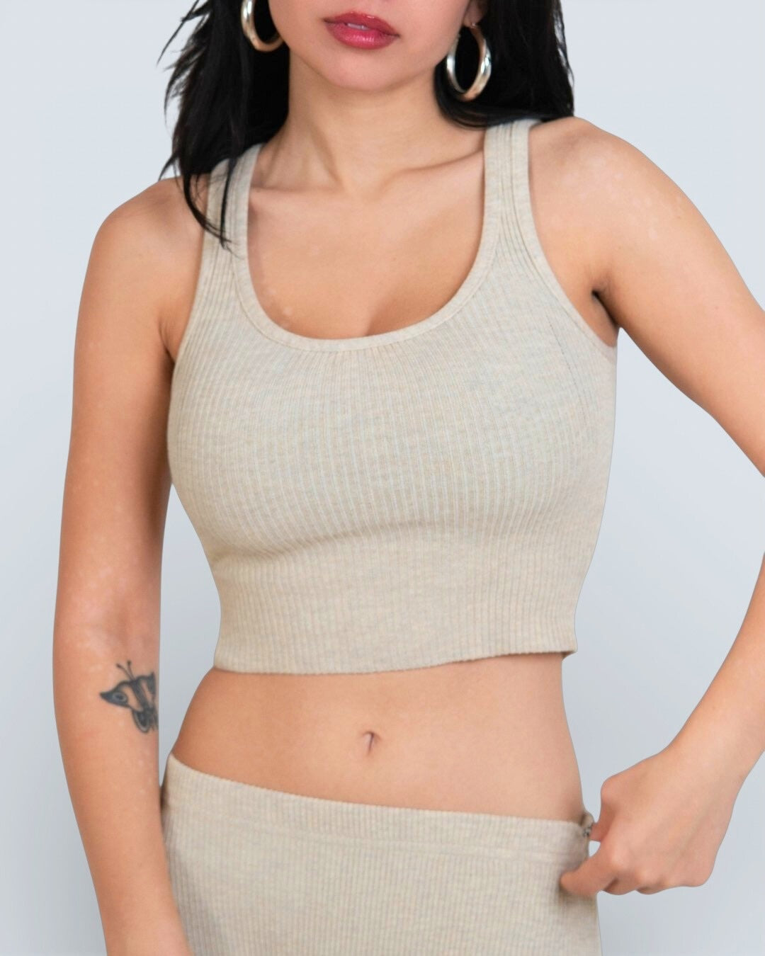 Woman wearing a beige ribbed scoop neck tank top against a light gray background