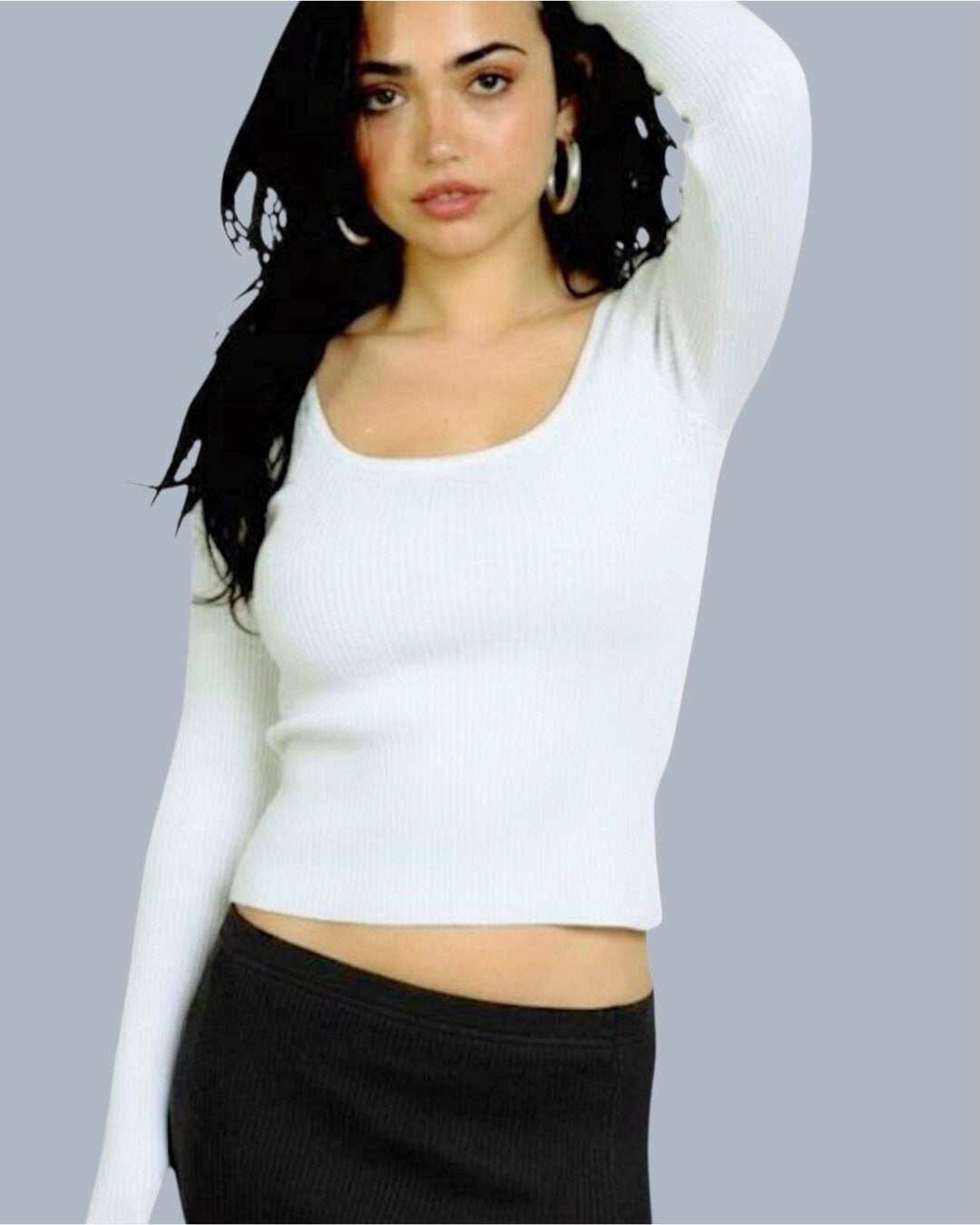Woman wearing a white long-sleeve scoop-neck top and black pants against a gray background
