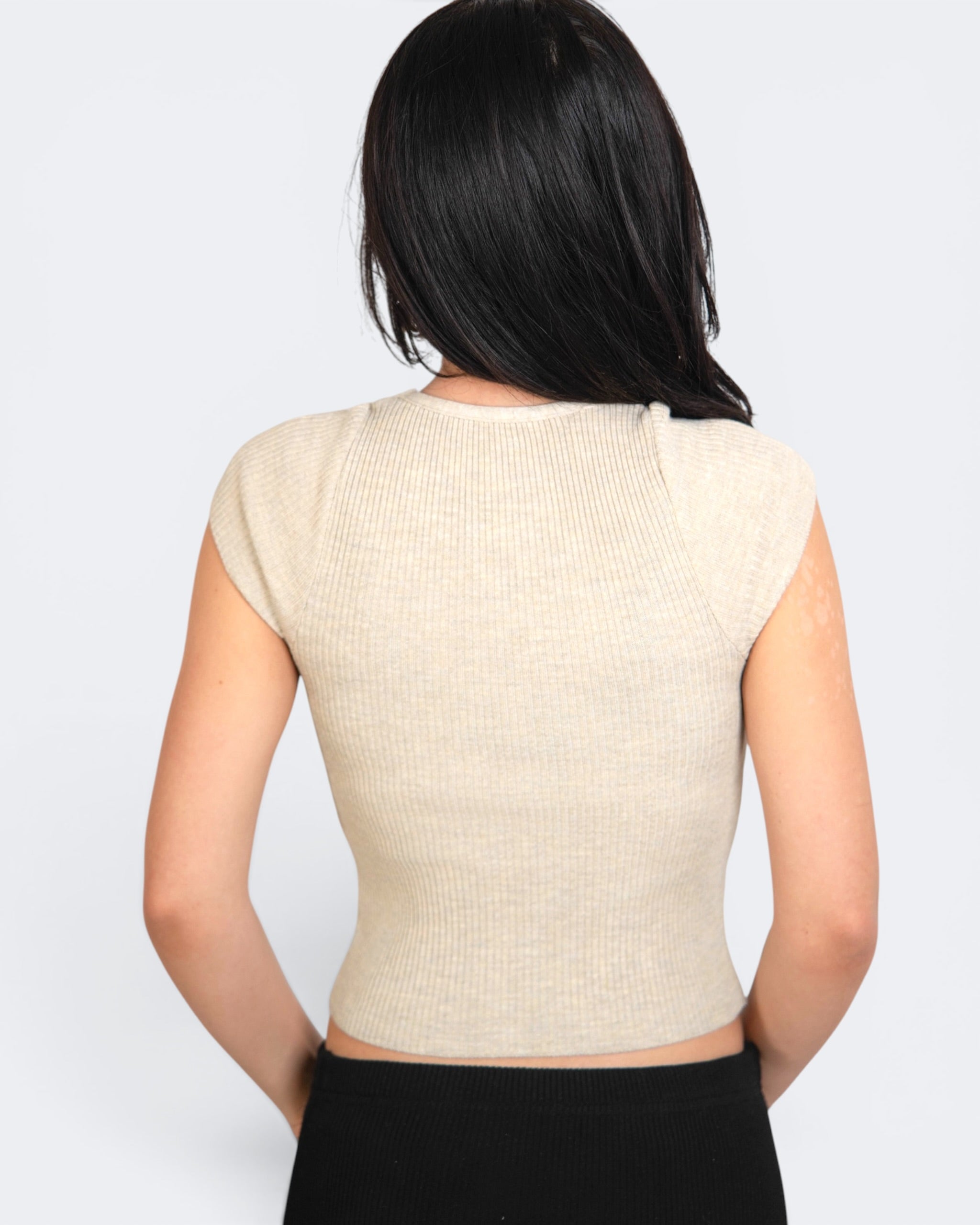 Woman wearing a beige sleeveless top against a white background