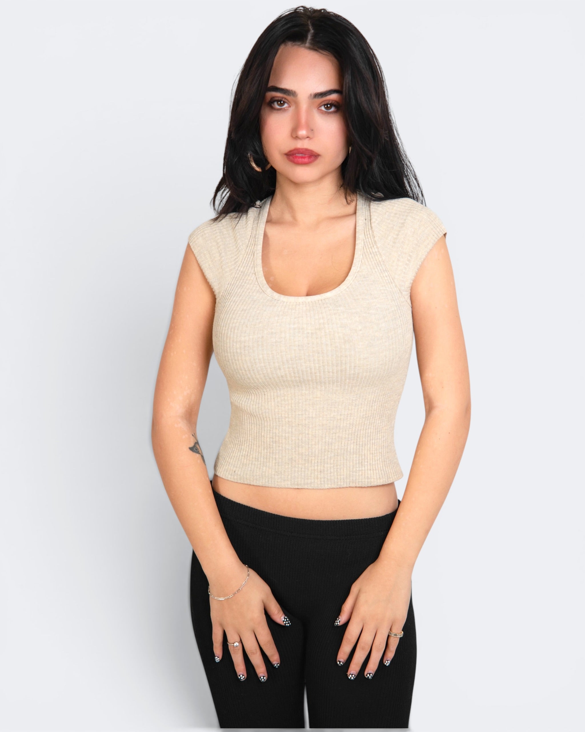 Woman wearing a beige cropped top and black pants on a white background