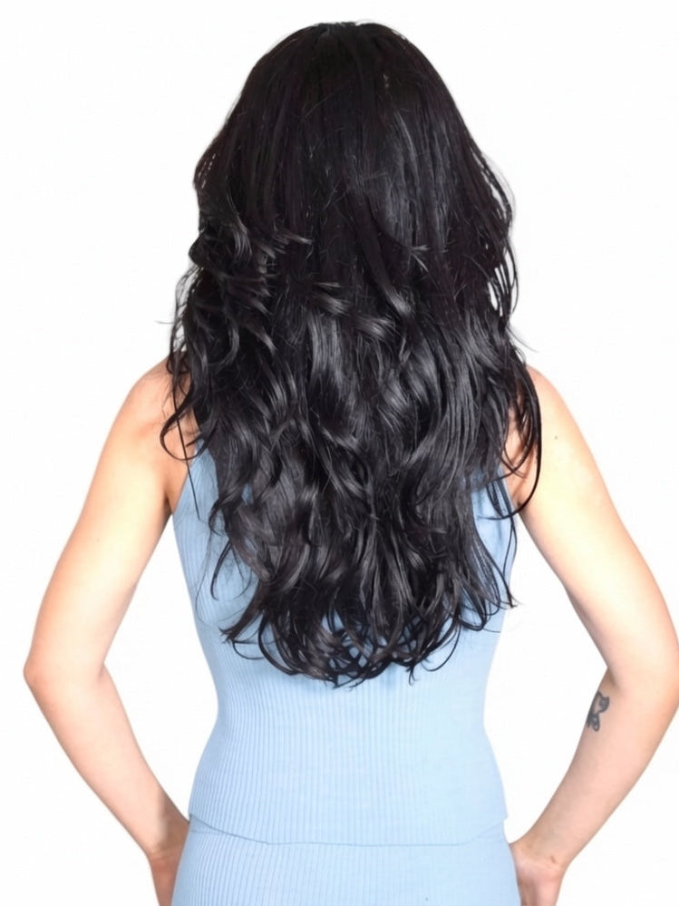 Person with long, wavy black hair wearing a light blue sleeveless top on a white background