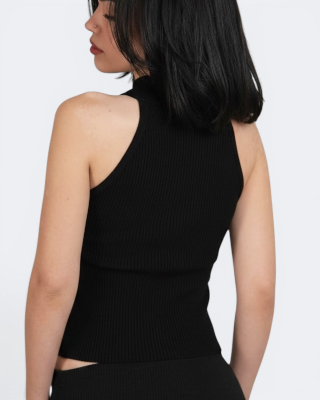 Woman wearing a black sleeveless top with cutout design on a white background