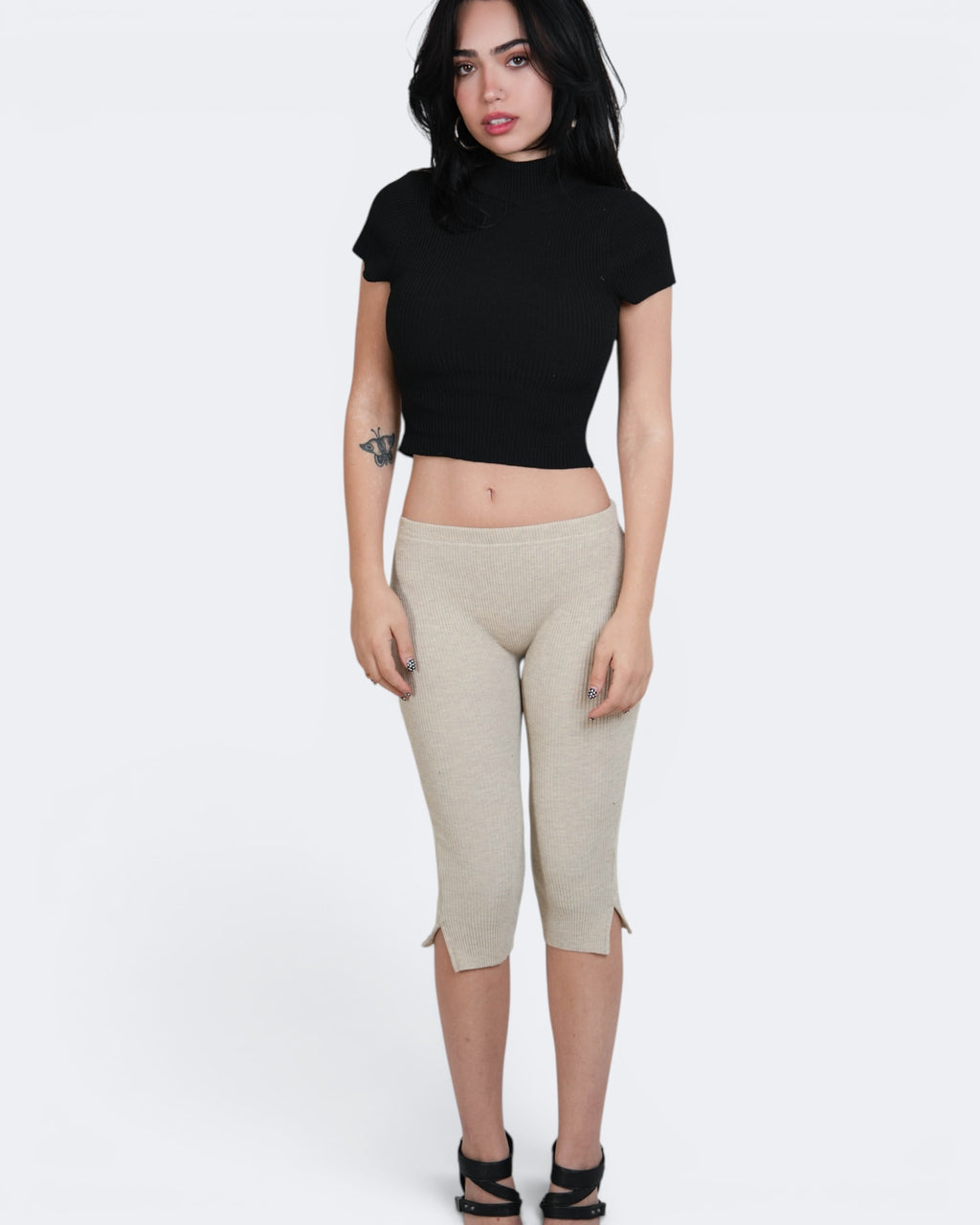 Woman wearing a black crop top and beige capri pants on a white background