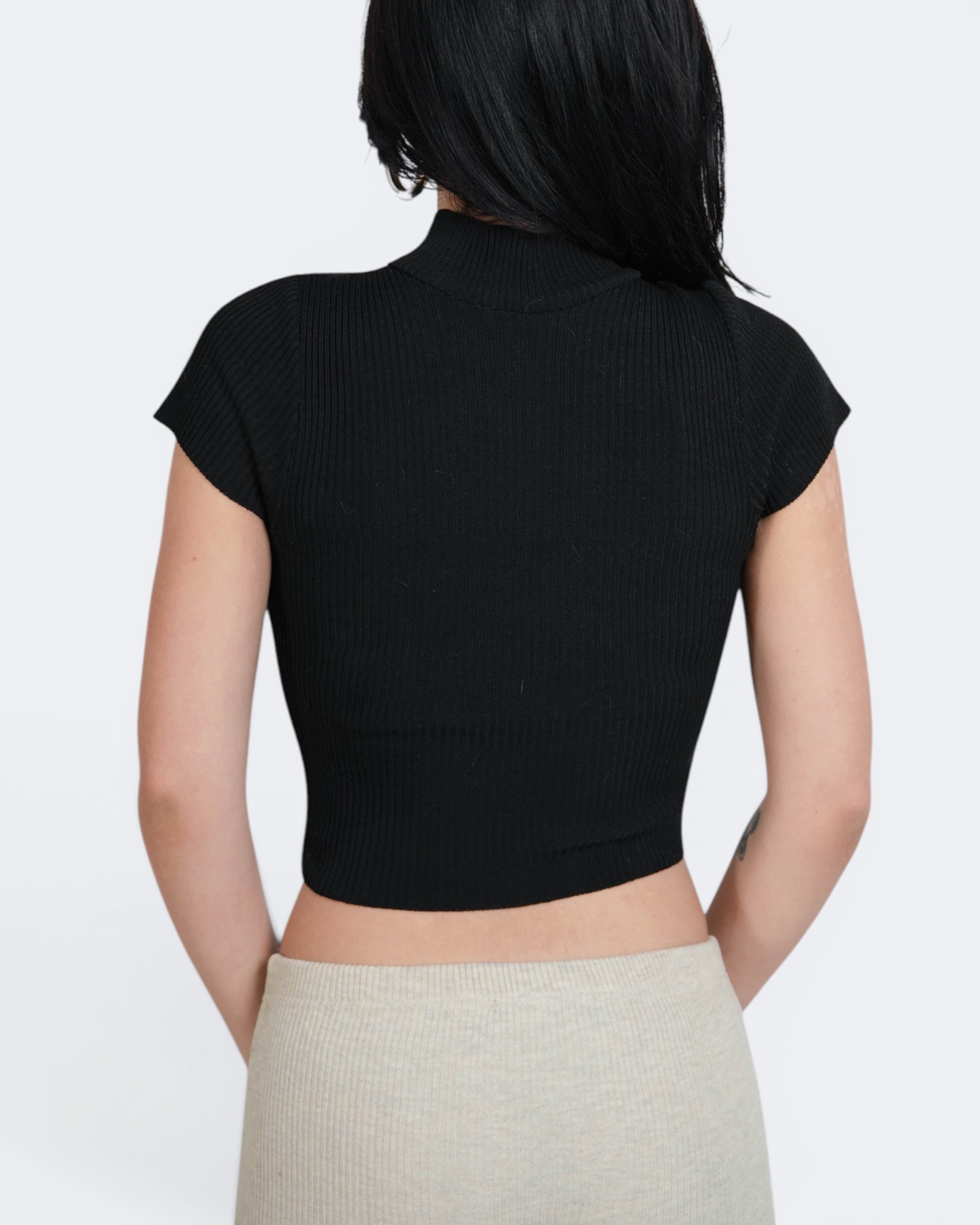 Person wearing a black ribbed crop top and beige pants on a white background