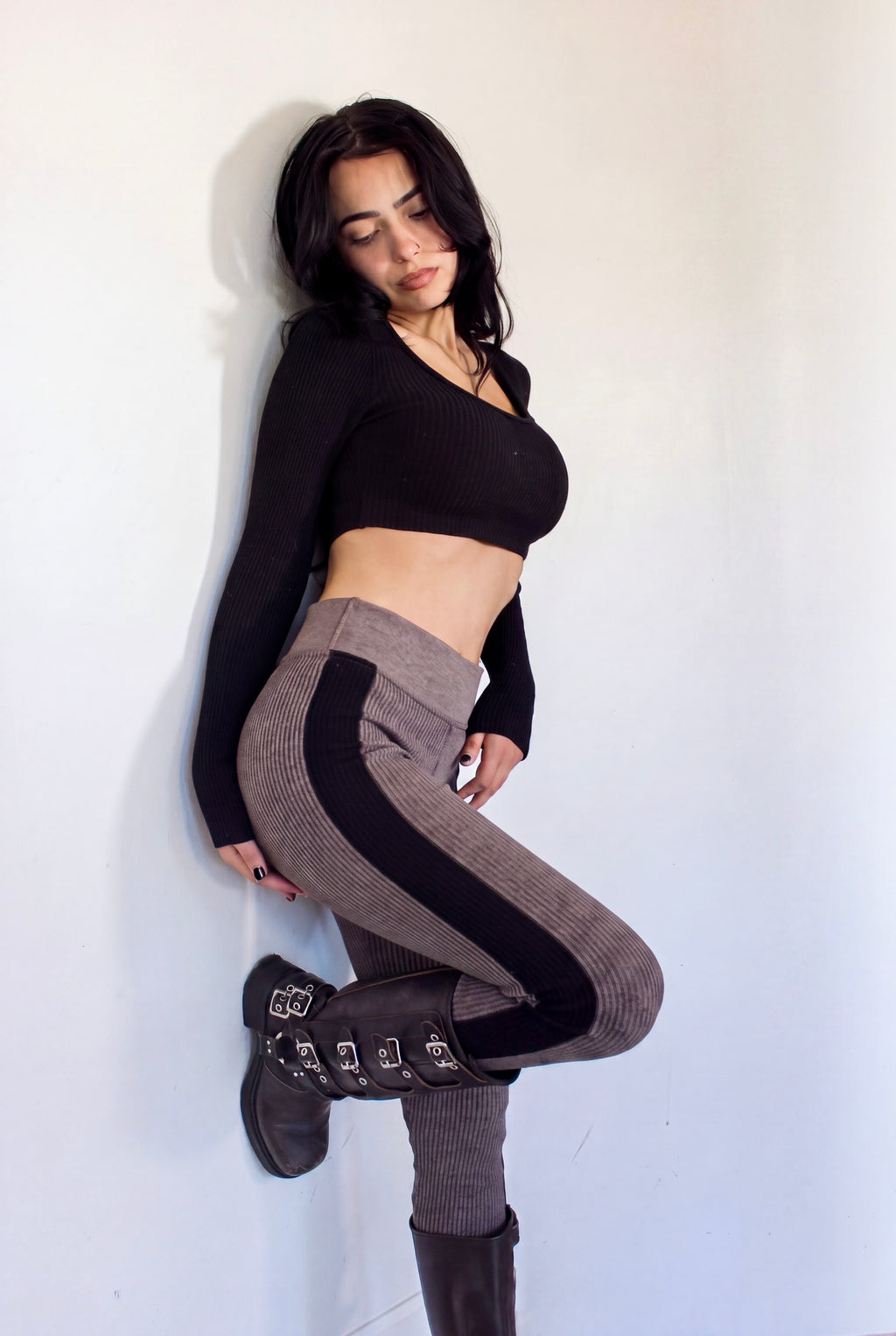 Woman leaning w knee bent wearing leggings in plum brown with black side stripe and black crop long sleeve scoop neck top by TKHLA 