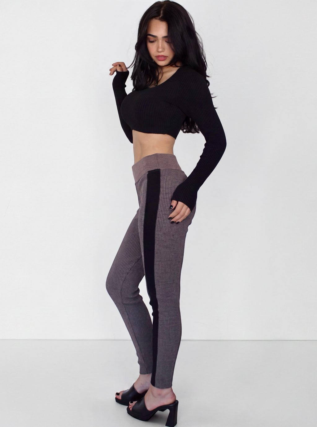 Woman wearing rib knit leggings in plum brown with black side stripe and a black crop long sleeve scoop neck top by TKHLA. 