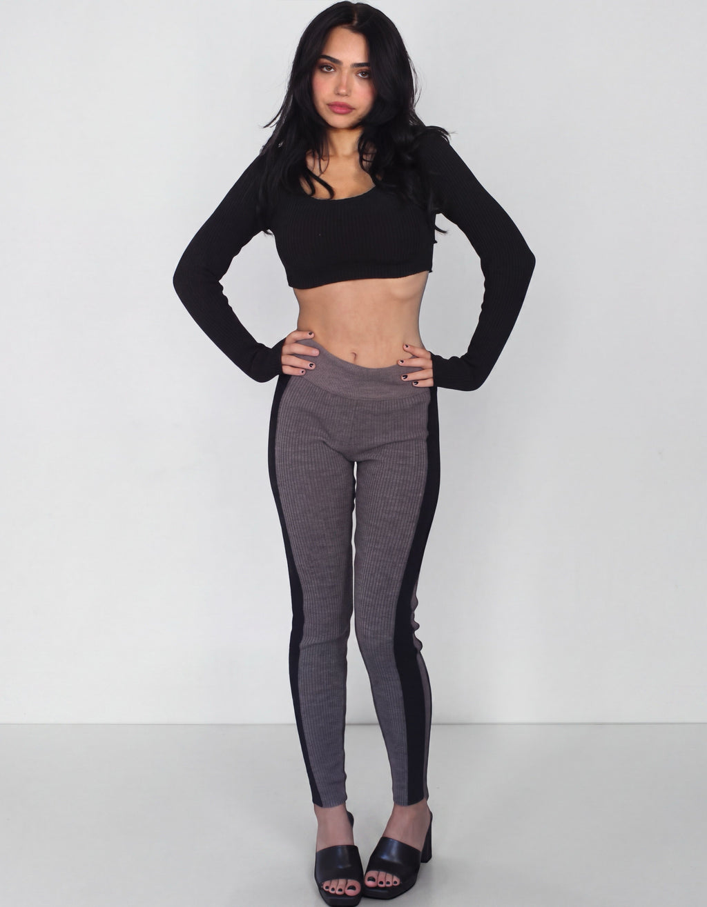 Woman wearing leggings in brown rib knit leggings with black side stripe and a black crop long sleeve scoop neck Top by TKHLA 