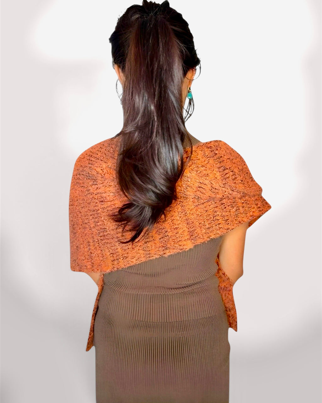 A woman shown from the back wearing a textured orange knit shawl draped over her shoulders and a brown ribbed dress, against a plain light background.