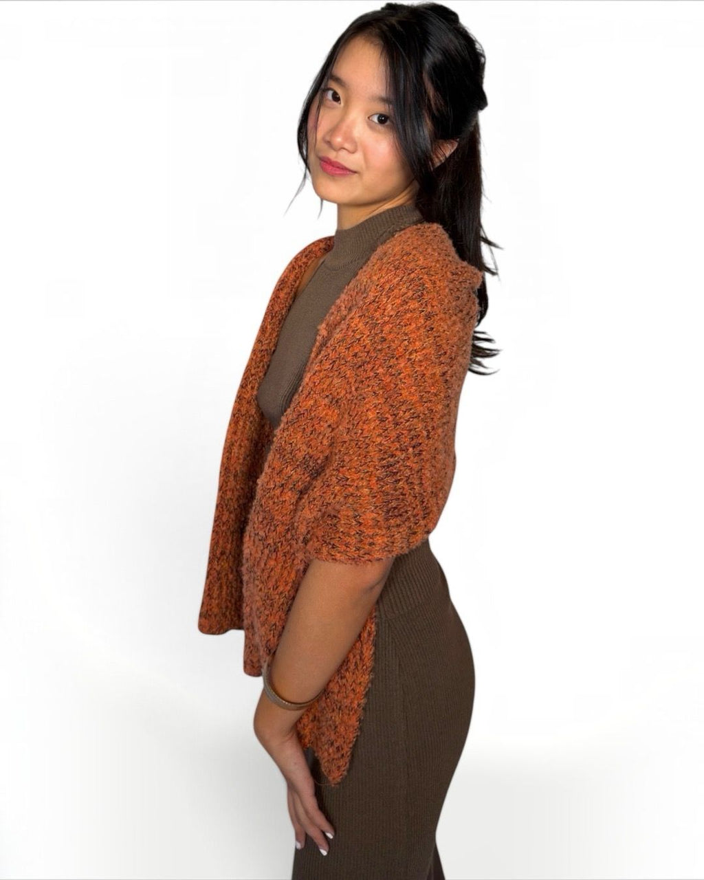 A woman wearing a textured orange and brown knit cardigan over a brown mock neck top and brown ribbed skirt, photographed against a solid white background.