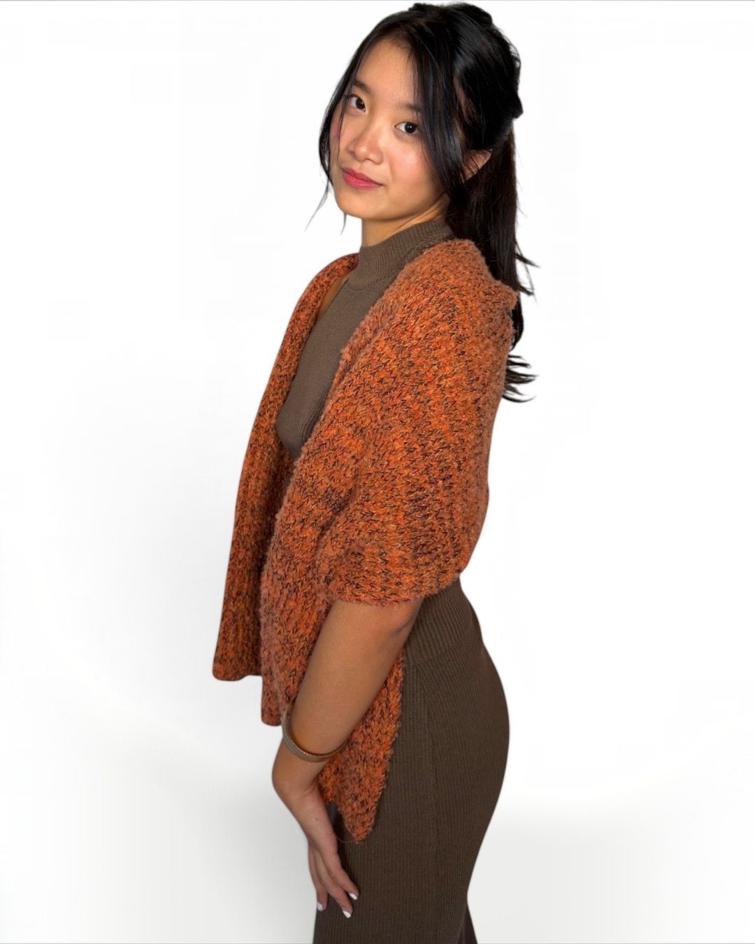 A woman wearing a textured orange and brown knit cardigan over a brown mock neck top and brown ribbed skirt, photographed against a solid white background.
