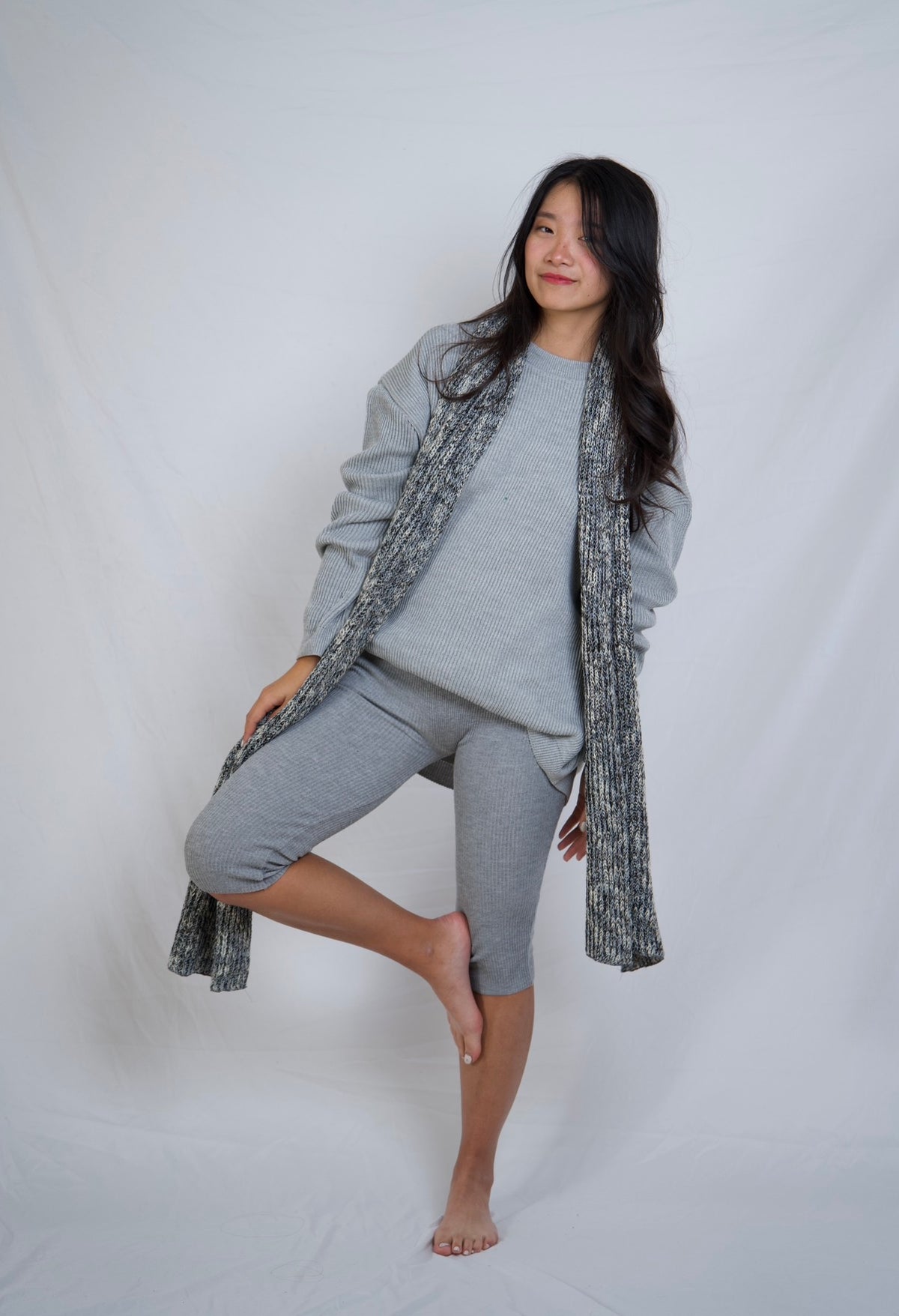 A woman modeling a gray lounge set consisting of a crewneck sweatshirt, matching capri pants, and a textured gray knit cardigan, posed against a white studio backdrop.