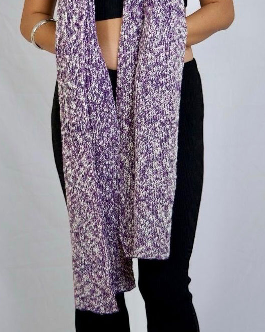 A woman modeling a long, lightweight scarf with a purple and white abstract floral pattern, styled over a black crop top and black pants against a light gray studio backdrop.