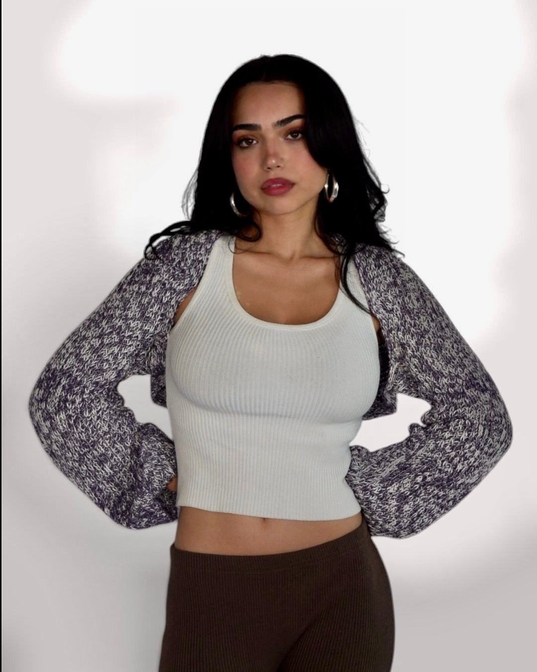 A woman modeling a white ribbed crop top with a long-sleeve, open-front knit cardigan featuring a gray and white marled pattern, paired with brown ribbed leggings, against a plain white studio background.