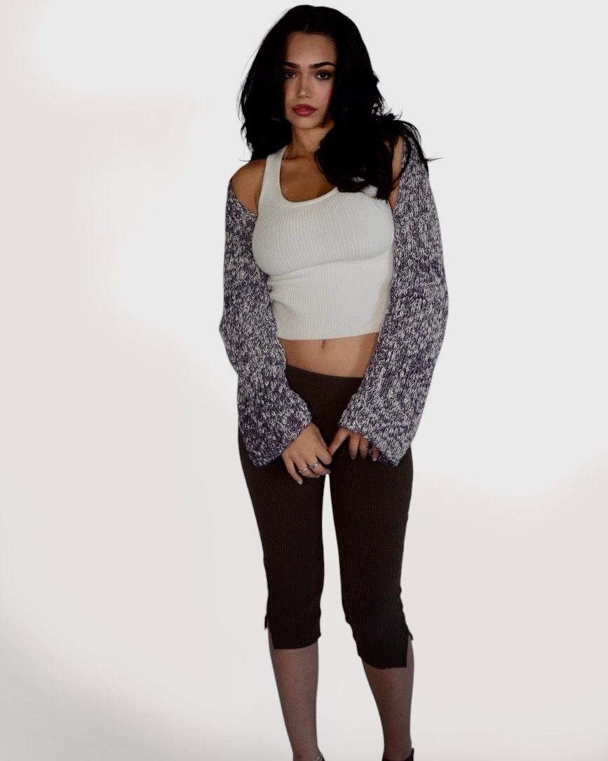 A woman modeling a white ribbed crop top with long, open-sleeve marled knit sleeves, paired with dark brown cropped leggings, against a plain white studio background.