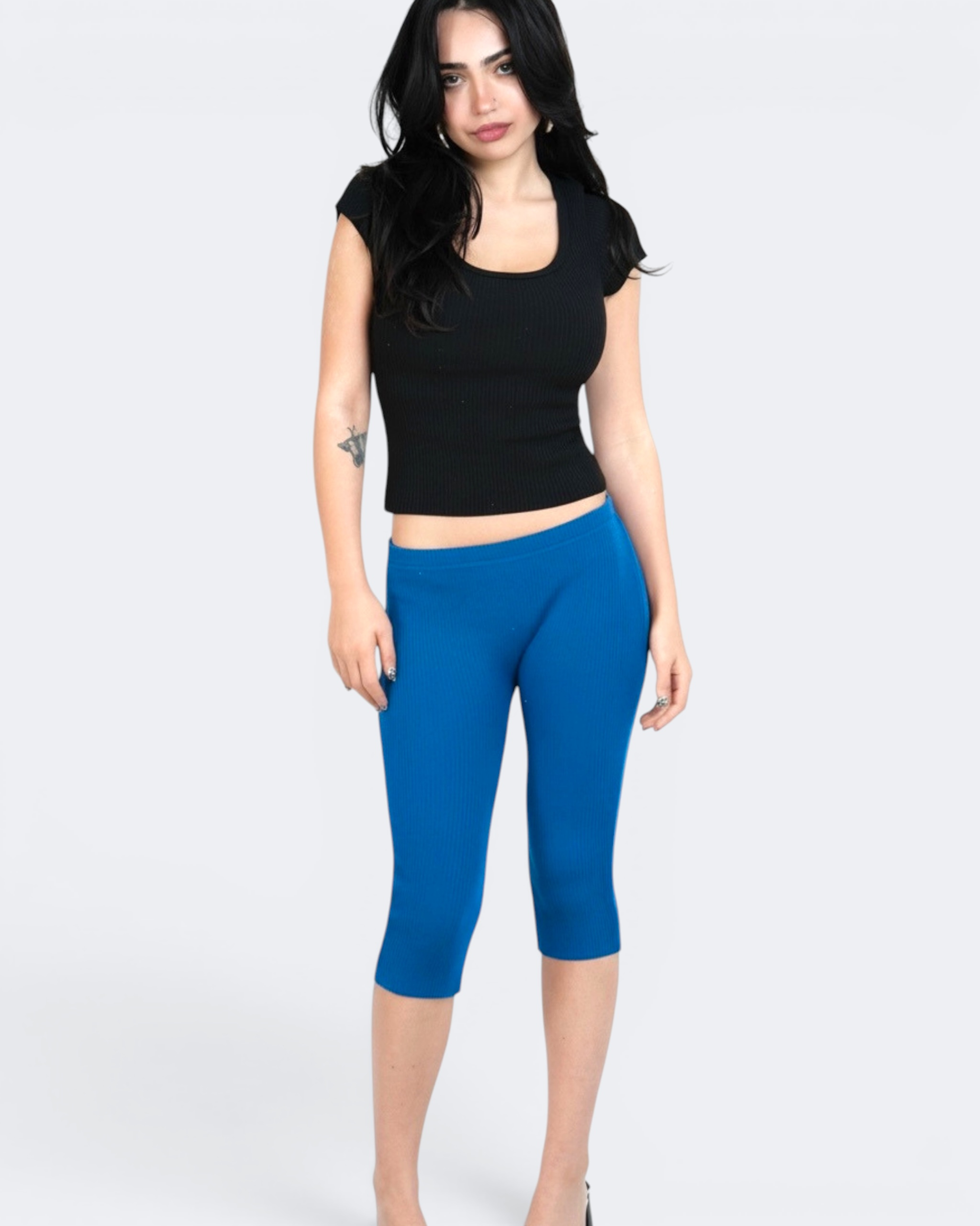 Woman wearing a black crop top and cobalt blue capri leggings on a white background