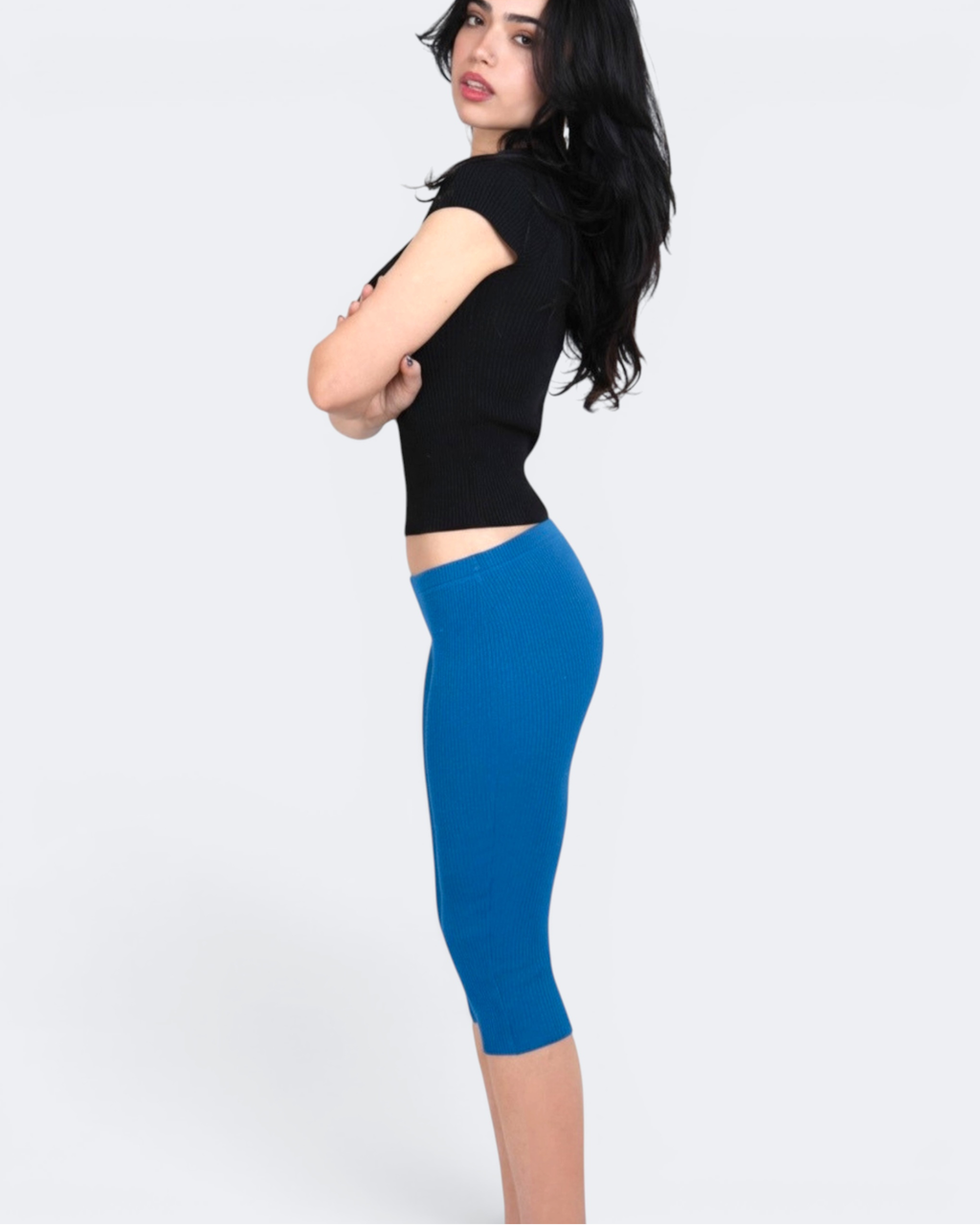 Woman wearing a black sleeveless top and cobalt blue capri leggings on a white background