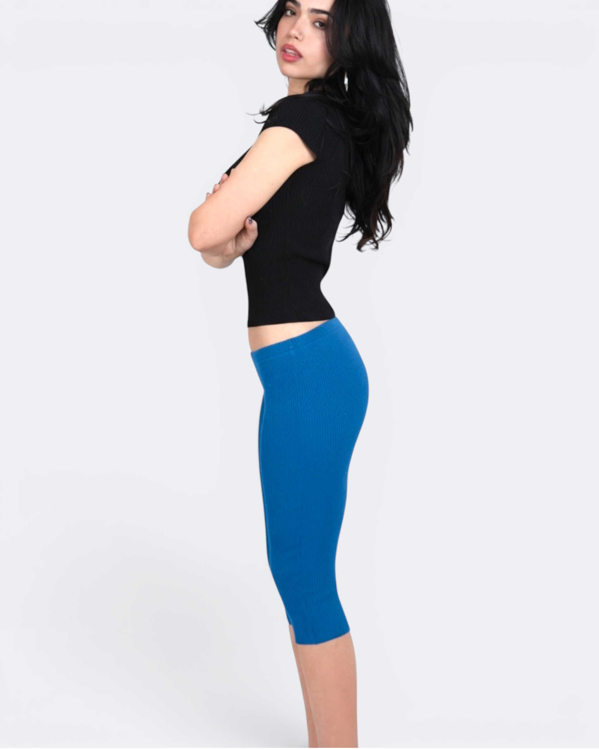 Woman wearing a black sleeveless top and cobalt blue capri leggings on a white background