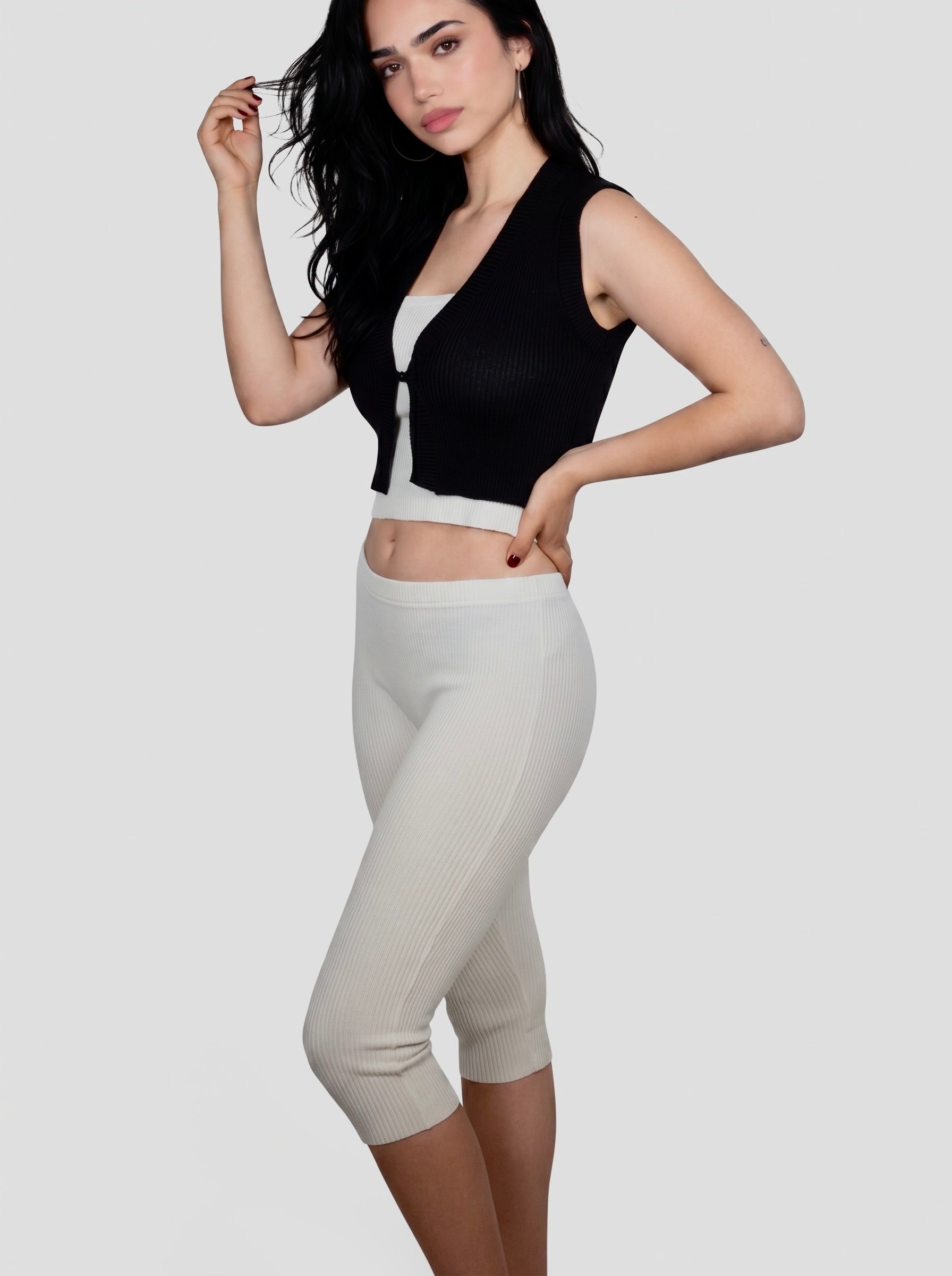 Woman wearing white rib knit Capri with white tube top and black semi sheer vest by TKHLA 