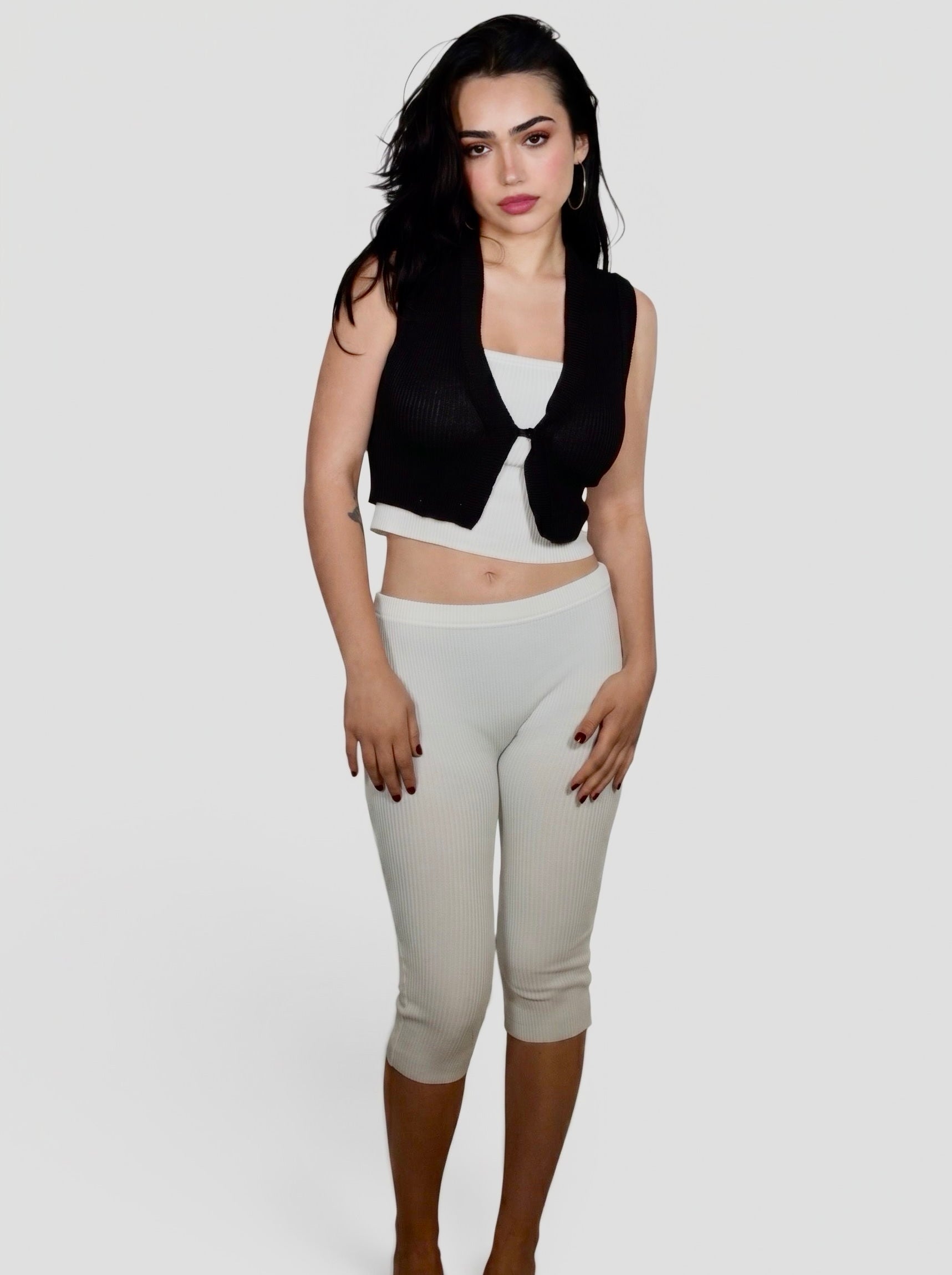 Woman wearing white rib knit tube top and Capri with black semi sheer vest by TKHLA 
