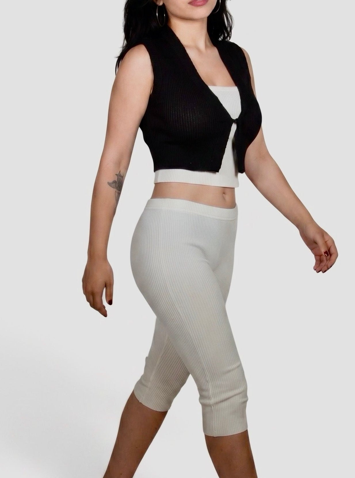 Woman walking wearing white rib knit tube top and Capri with black semi sheer vest by TKHLA 