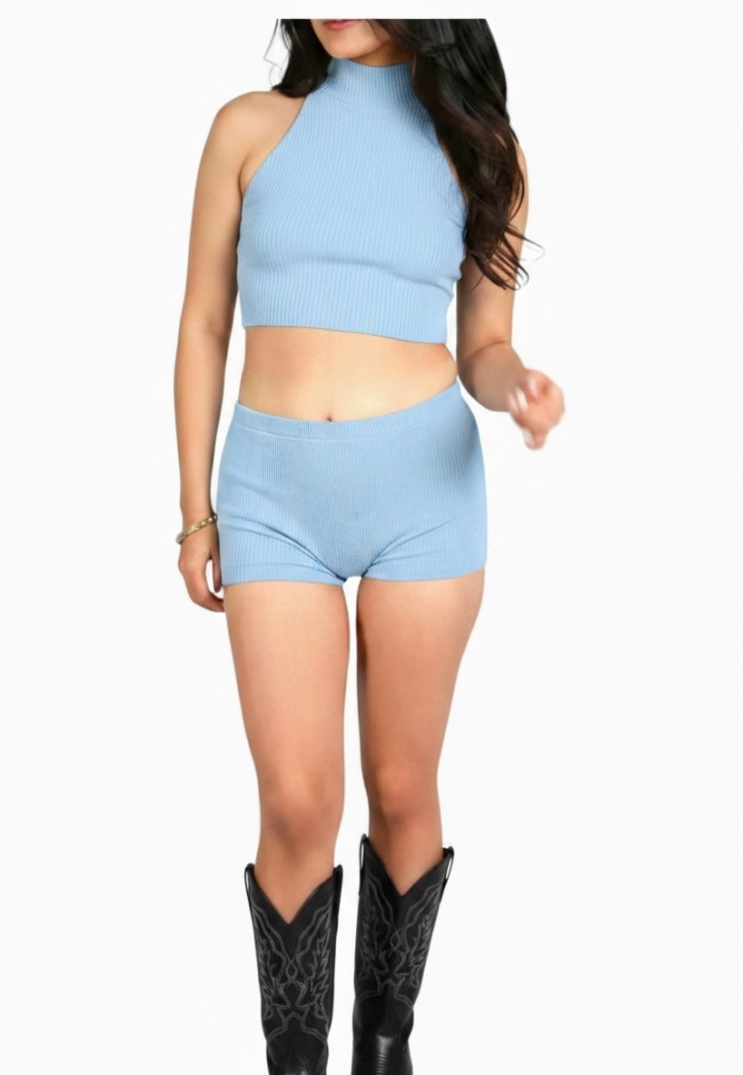 Woman wearing a light blue sleeveless top and shorts set with black cowboy boots on a white background