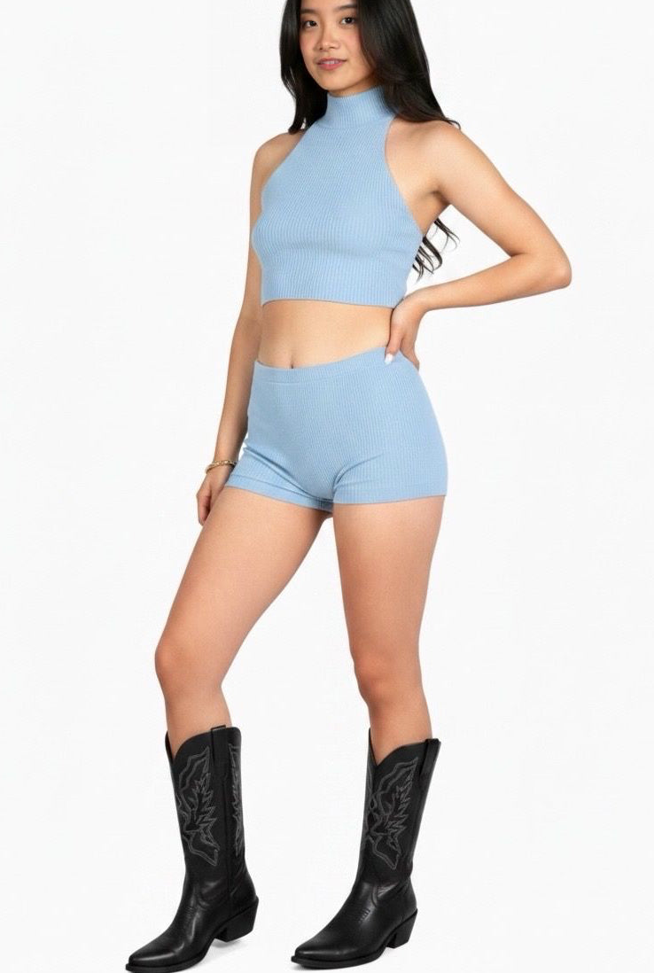 Woman wearing a light blue crop top and shorts set with black boots on a white background