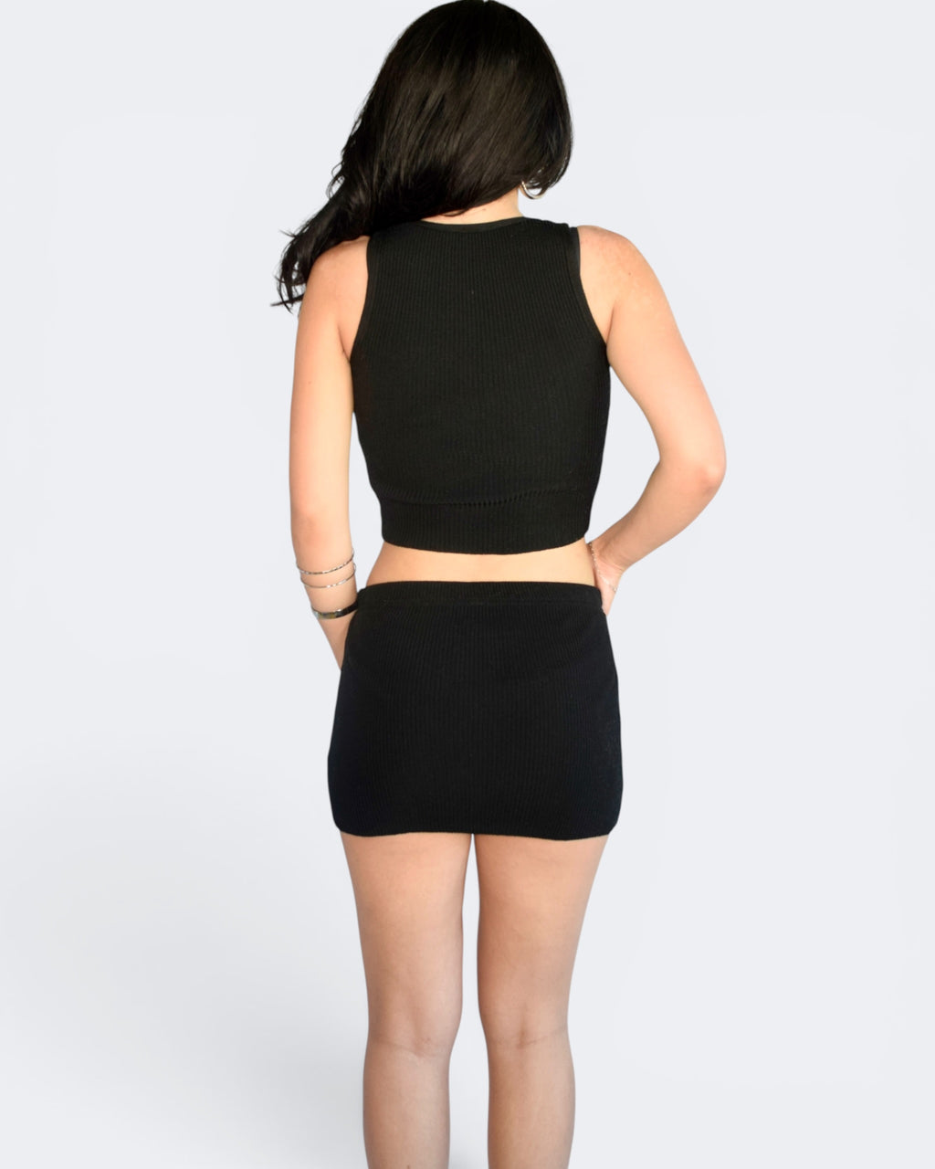 Person wearing a black sleeveless top and skirt set on a white background