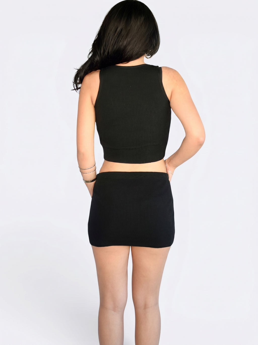 Person wearing matching black rib knit crop tank and mini skirt by TKHLA 