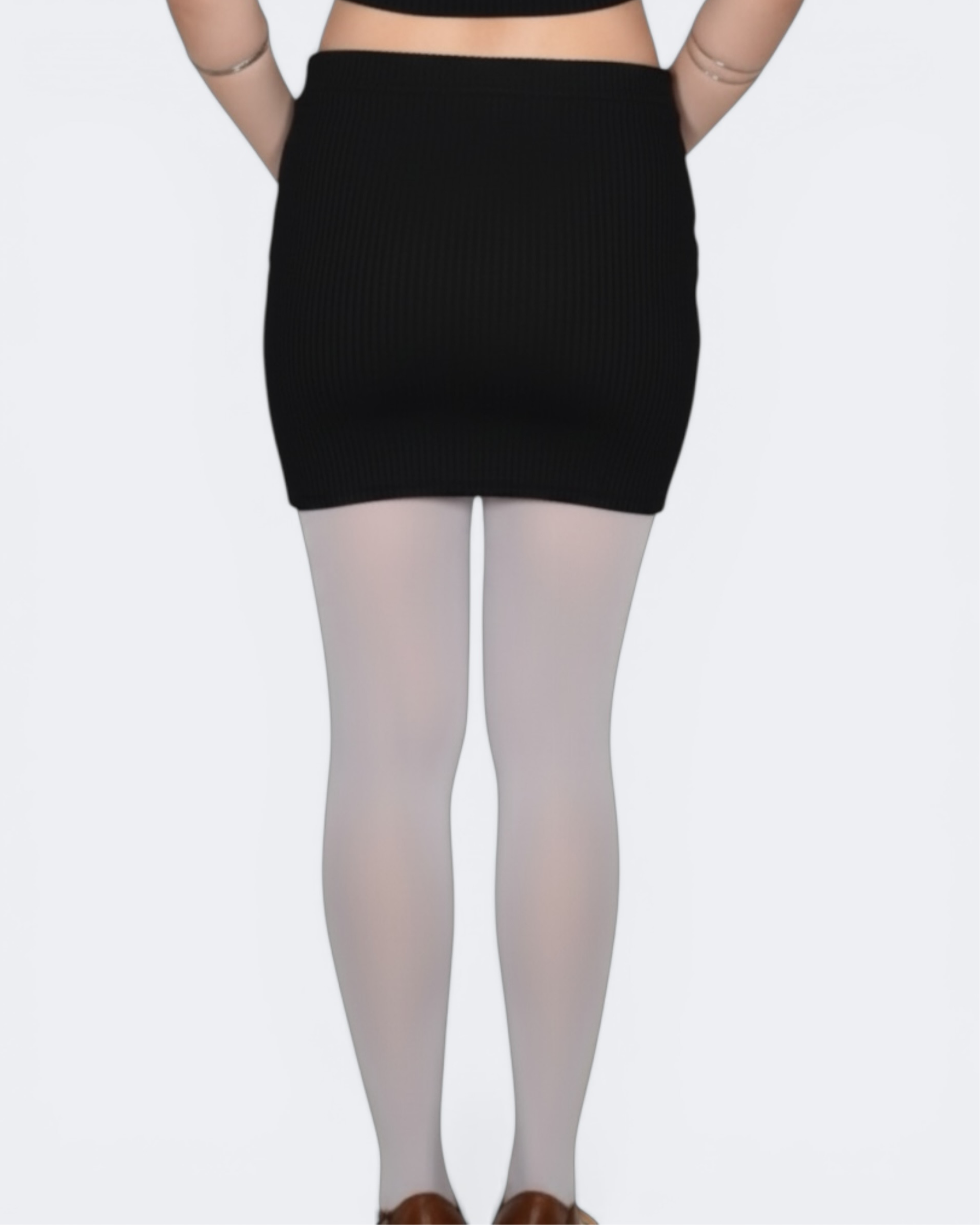 Person wearing a black ribbed skirt and white tights on a plain background