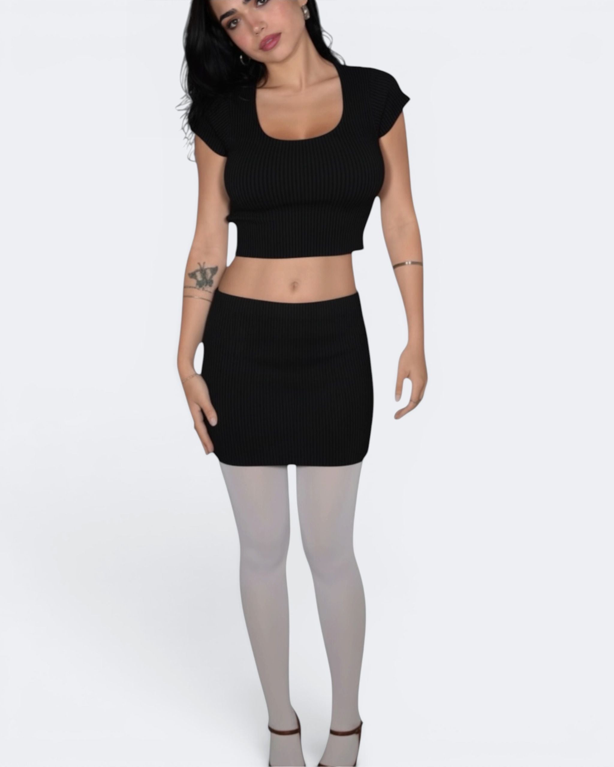 Person wearing a black crop top and skirt with white tights on a white background