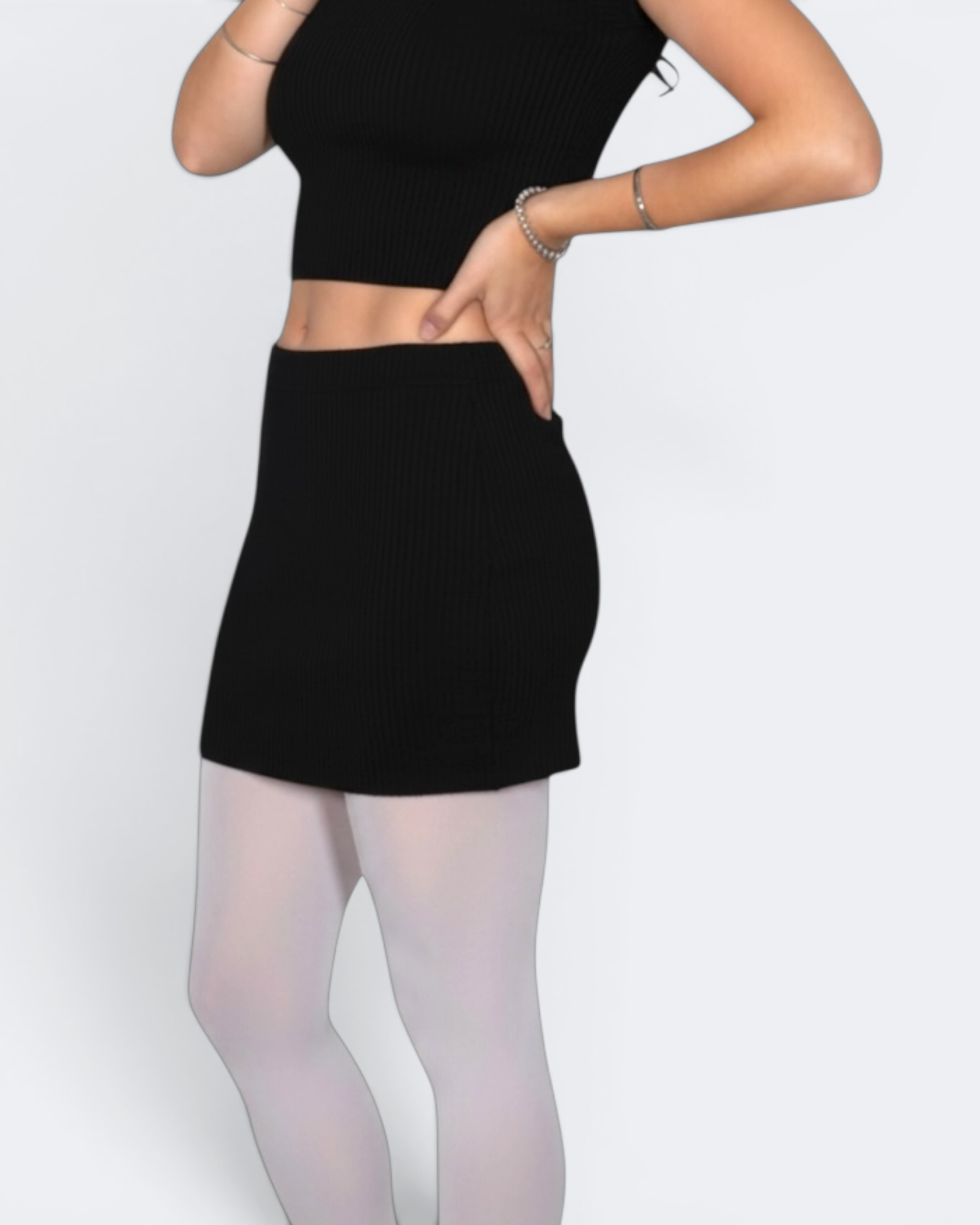 Person wearing a black crop top and black mini skirt with white tights on a light gray background