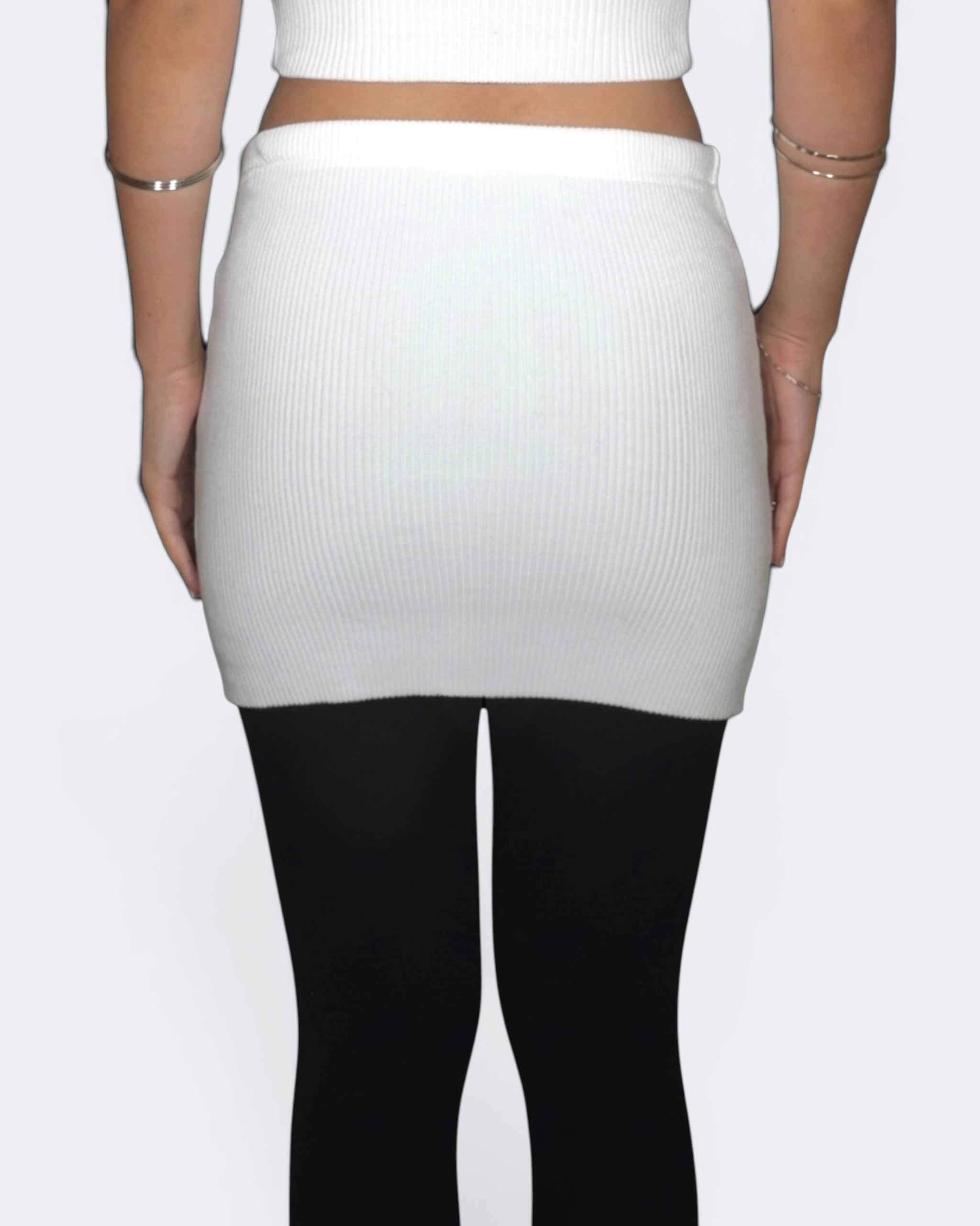 Person wearing a white ribbed skirt and black tights on a plain background
