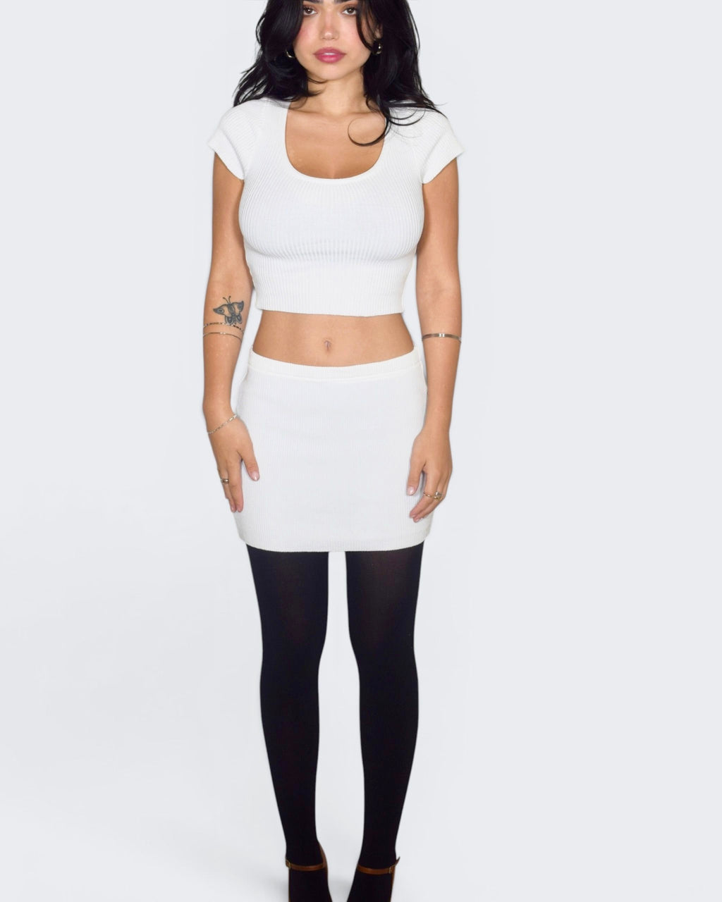 Person wearing a white crop top and skirt with black tights on a plain background