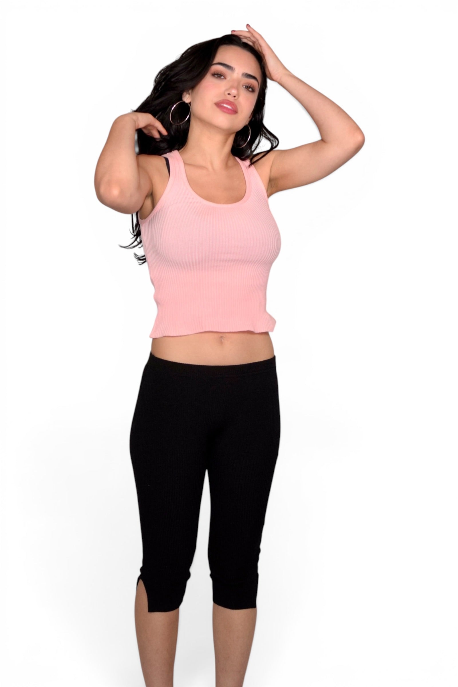Woman wearing a pink tank top and black capri pants on a white background