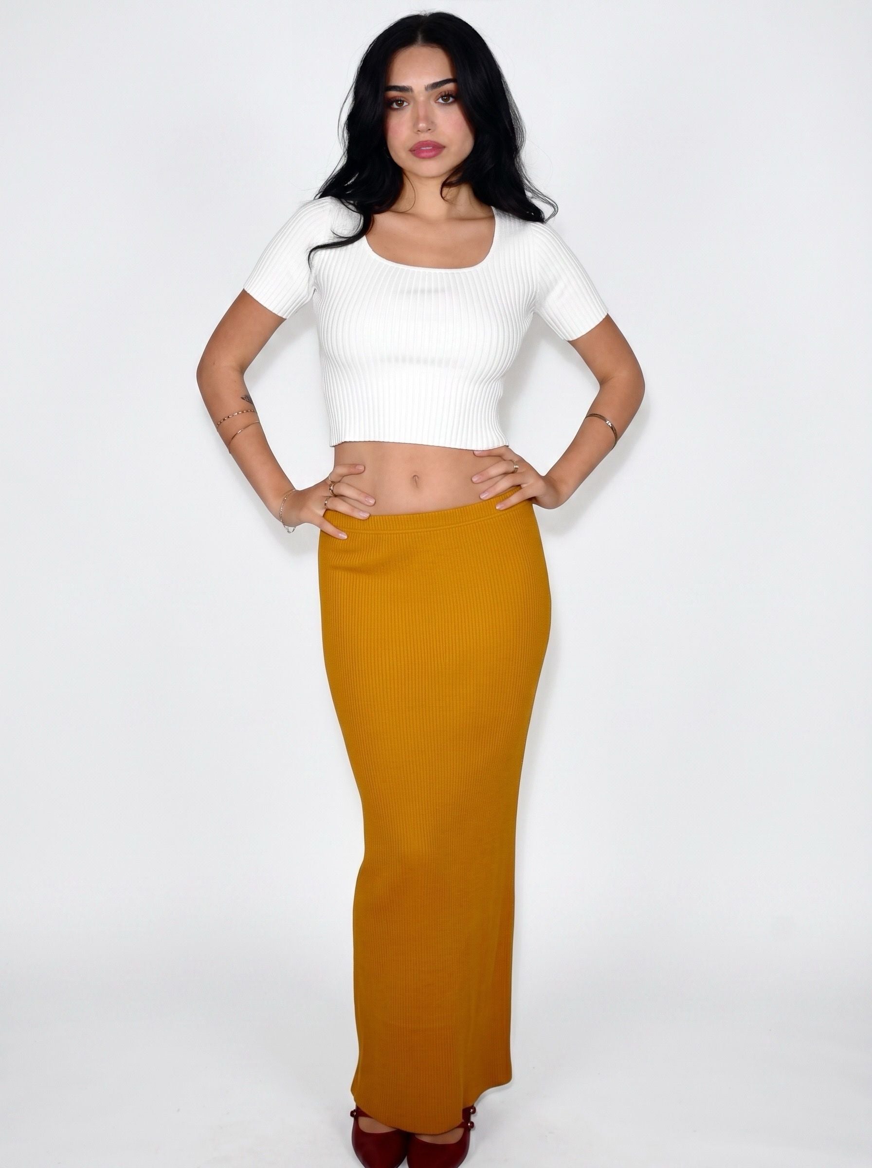 Woman wearing white rib knit crop top and mustard long straight skirt by TKHLA 