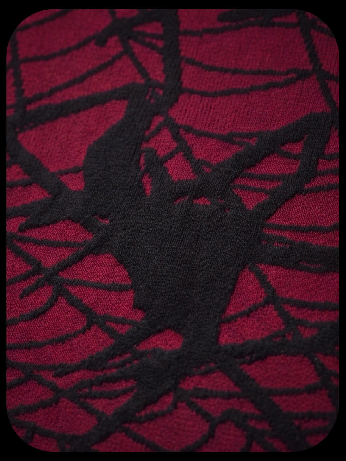 A close-up of a red knit fabric with a black spiderweb pattern and a large black spider motif in the center.