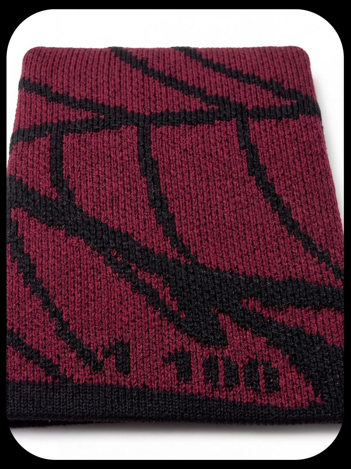 A close-up of a folded knit swatch in deep burgundy with a black geometric pattern and black ribbed trim.