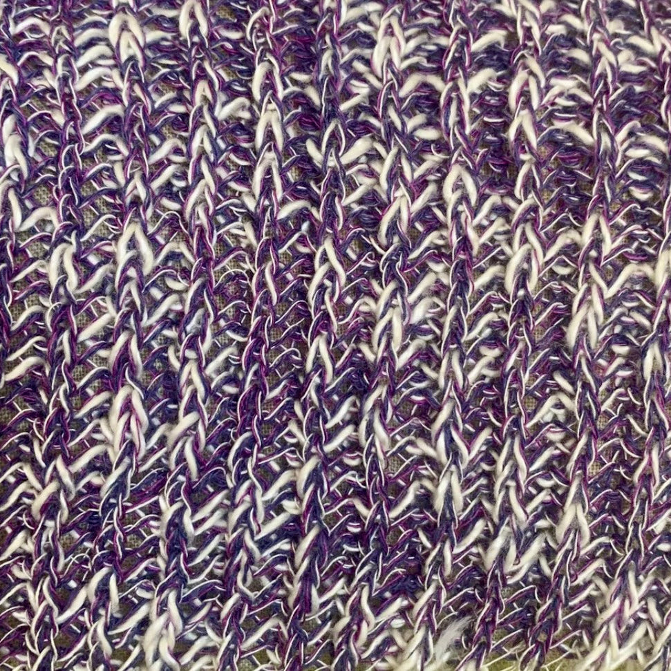 Close-up of a textured knit fabric with a variegated pattern of purple, white, and gray yarn.