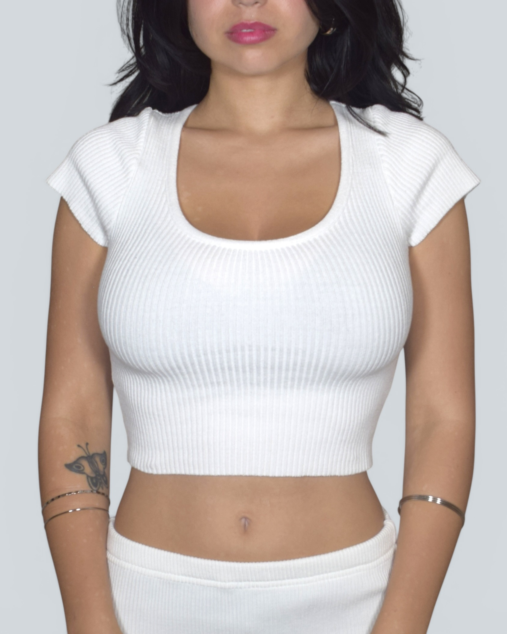 Person wearing a white ribbed crop top against a plain background
